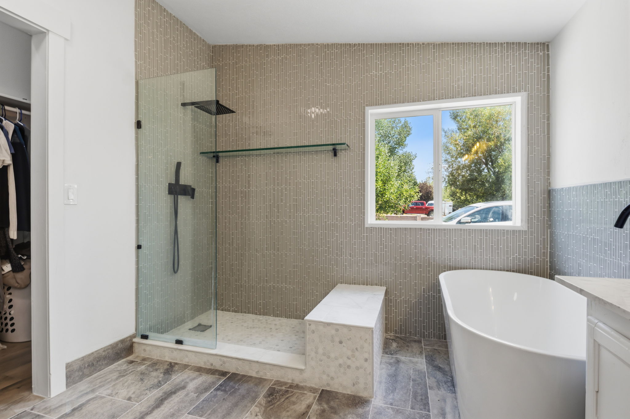 Modern bathroom featuring a freestanding soaking tub, a frameless glass shower enclosure with matte black fixtures, a built-in shower bench, and floor-to-ceiling tilework
