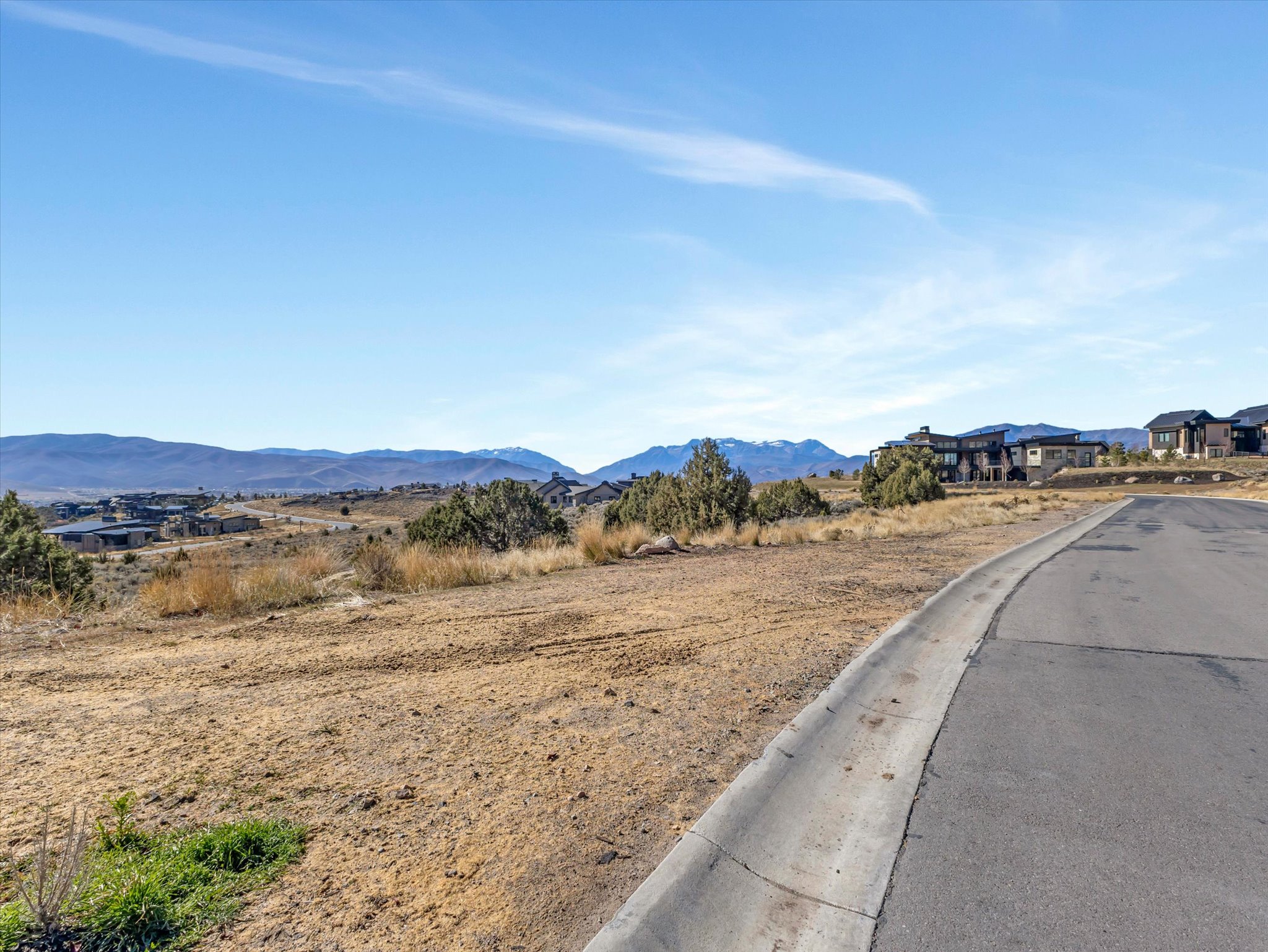 Expansive undeveloped land featuring a paved road, curb, and distant mountain scenery