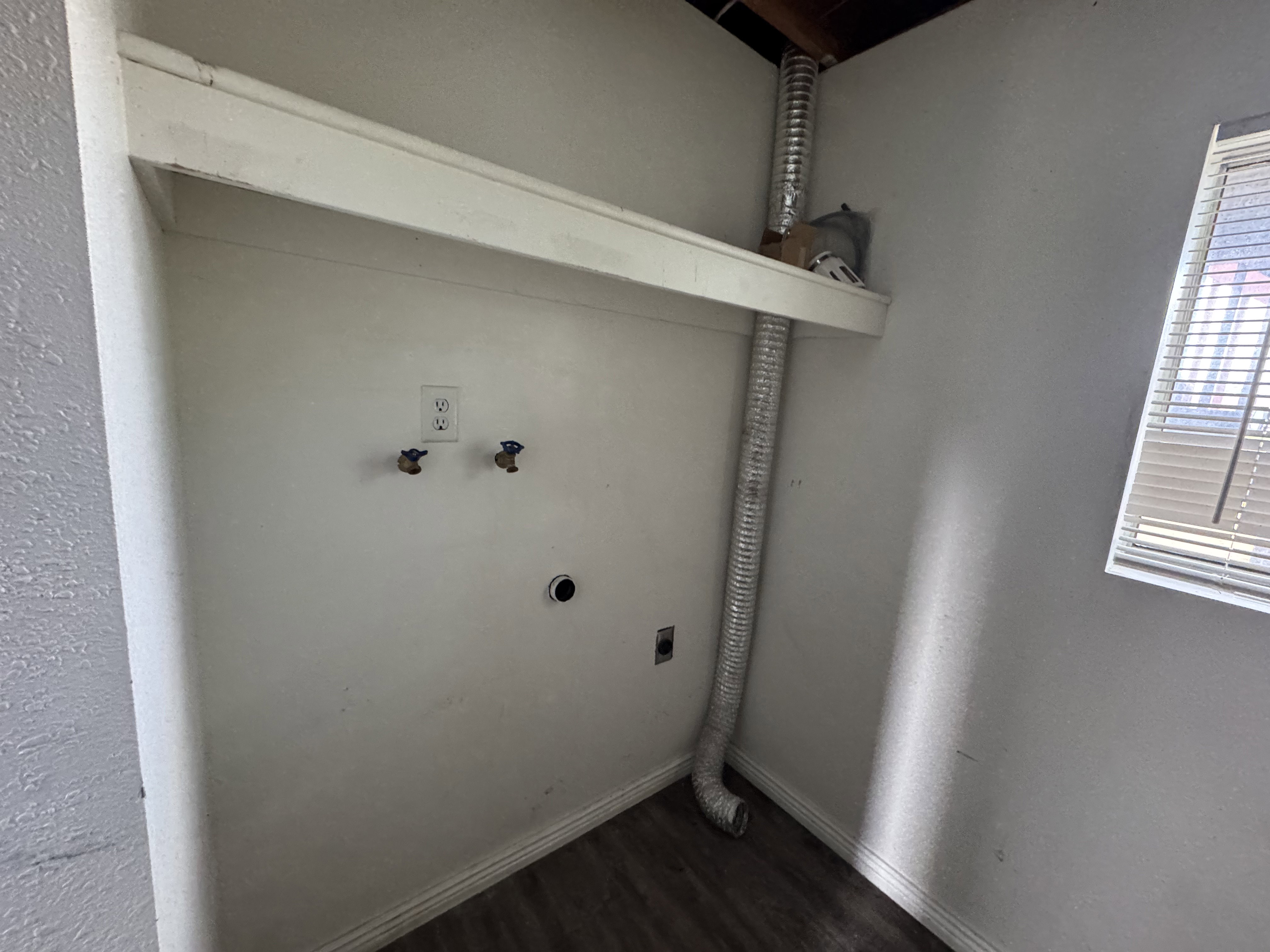 Dedicated laundry area featuring hookups for a washer and dryer, a utility shelf, wood-finish flooring, and natural light from a window with blinds