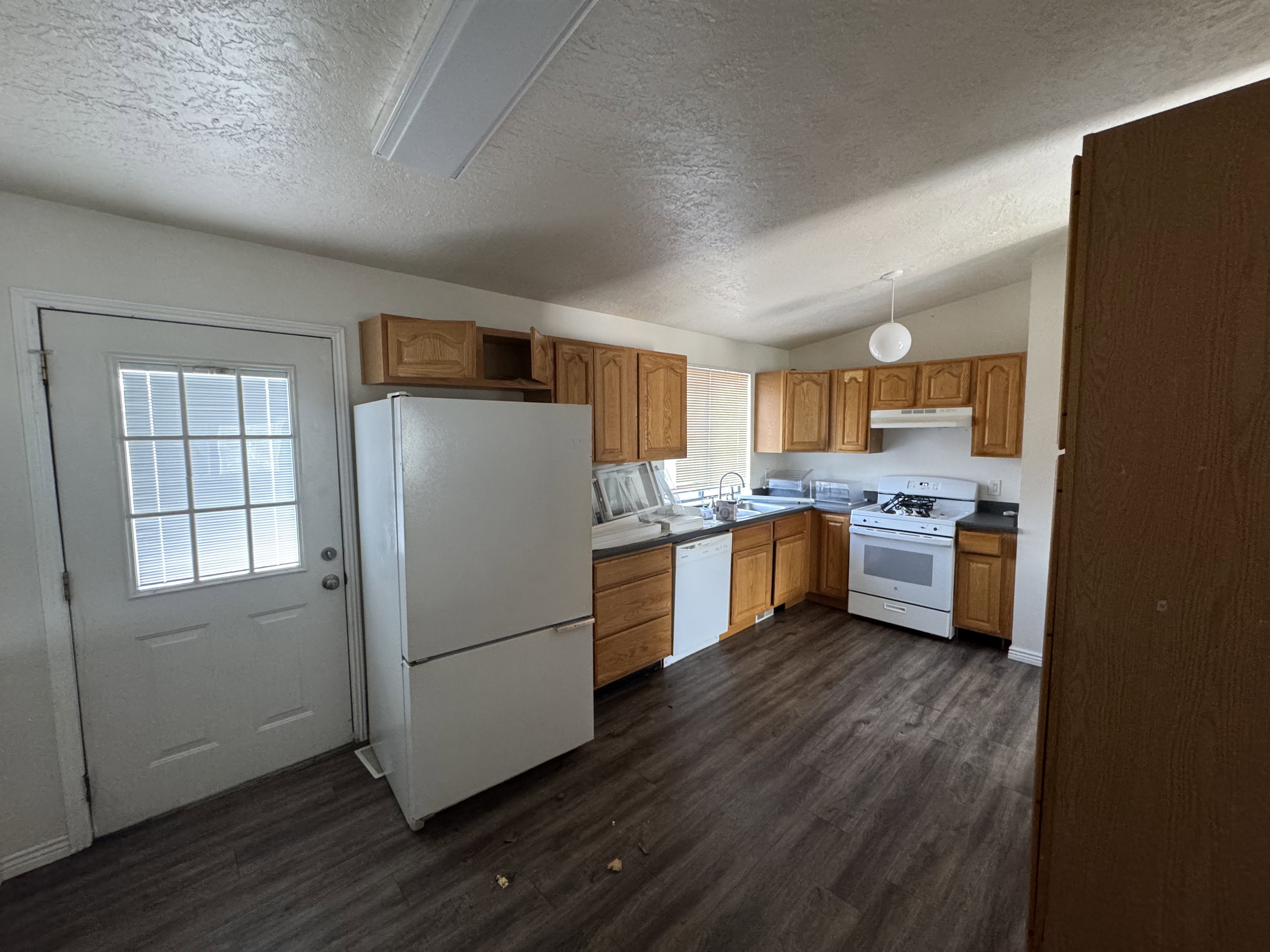Kitchen featuring wood-finish flooring, light wood cabinetry, white appliances, and dark countertops