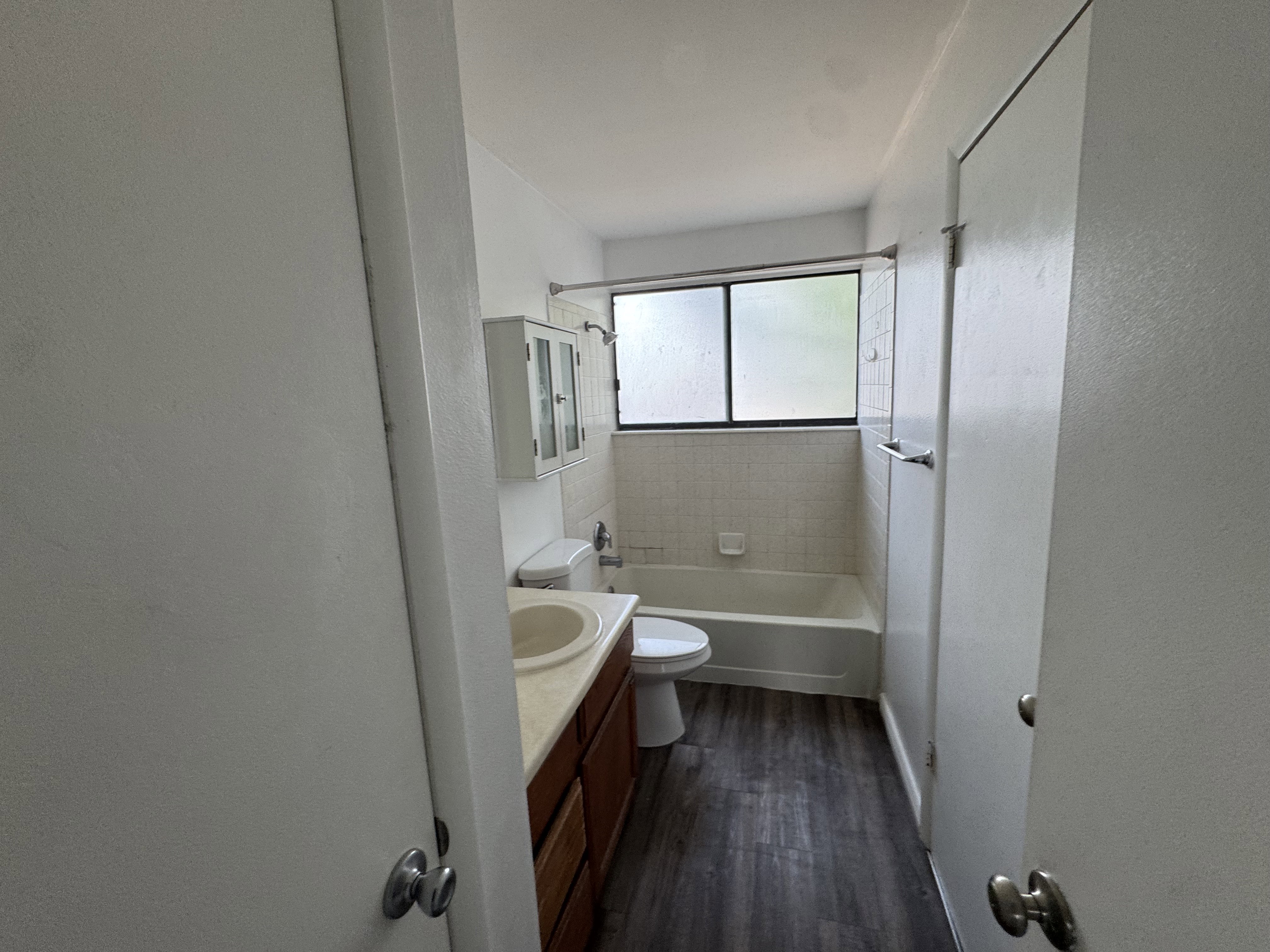 Bathroom featuring wood-finish flooring, a combined tub and shower with white tile surround, and a vanity with an integrated sink and wood-finish cabinetry