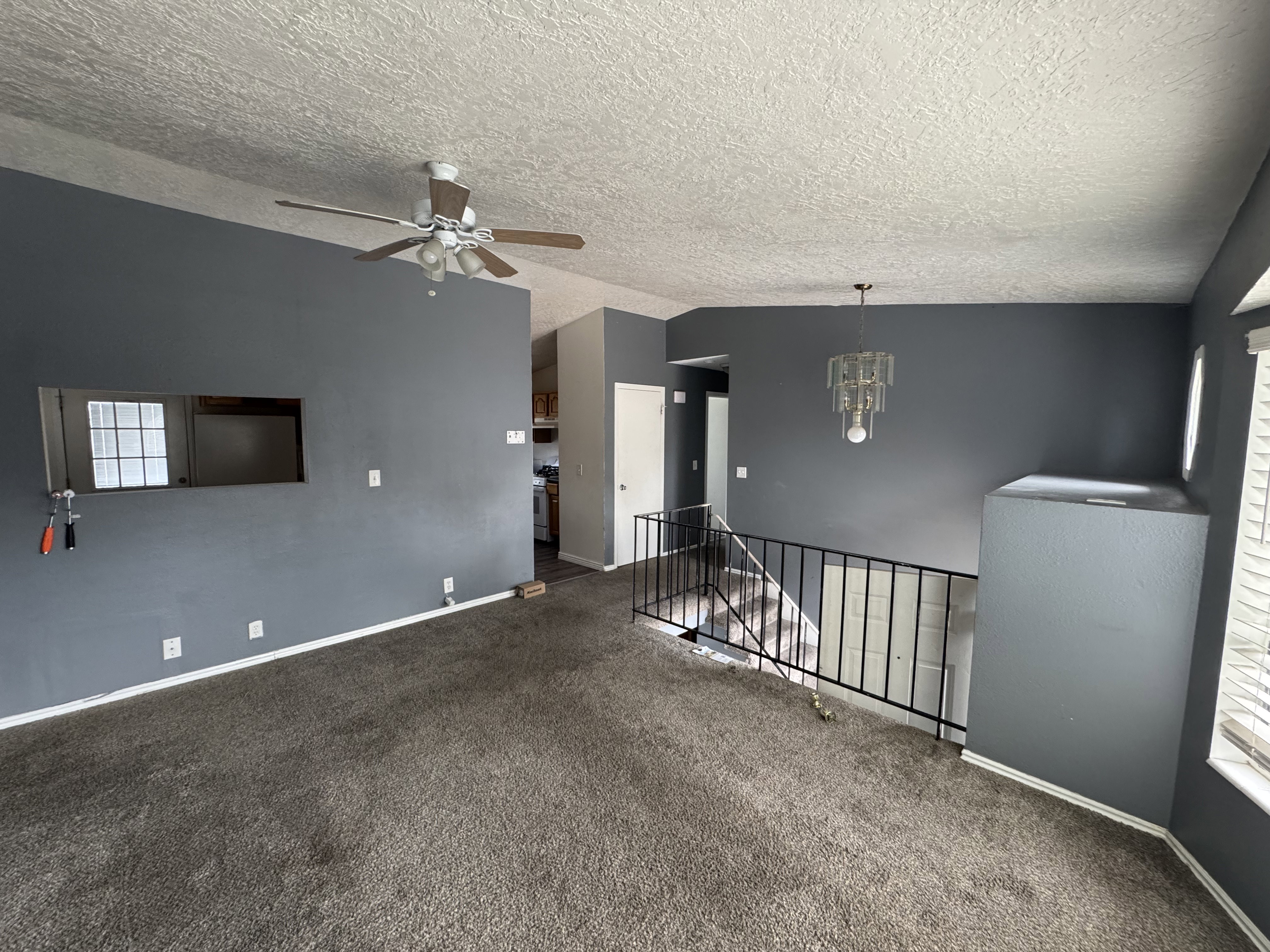 Open-concept living area featuring a ceiling fan, updated light fixture, interior window, and dark gray walls