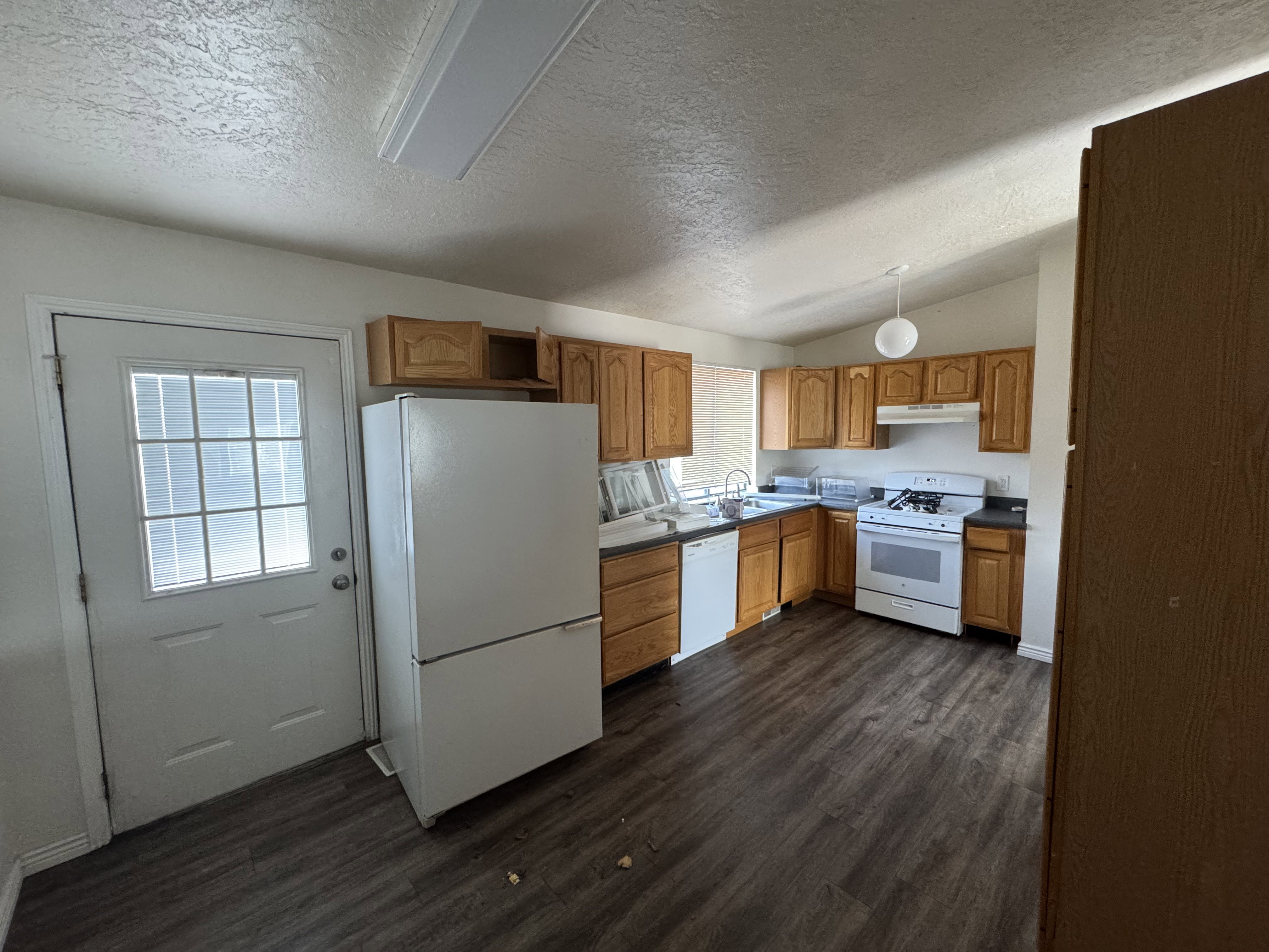 Kitchen featuring wood-finish flooring, light wood cabinetry, a white gas range, white dishwasher, and dark countertops