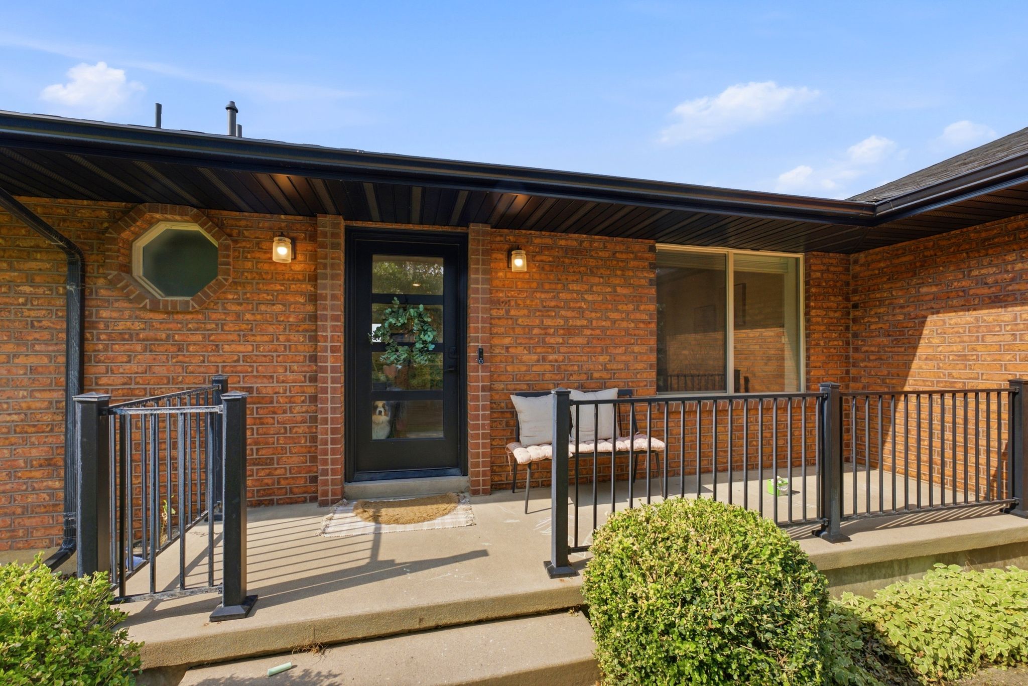Brick exterior featuring a covered entry, black metal railing, and a modern black entry door with frosted glass