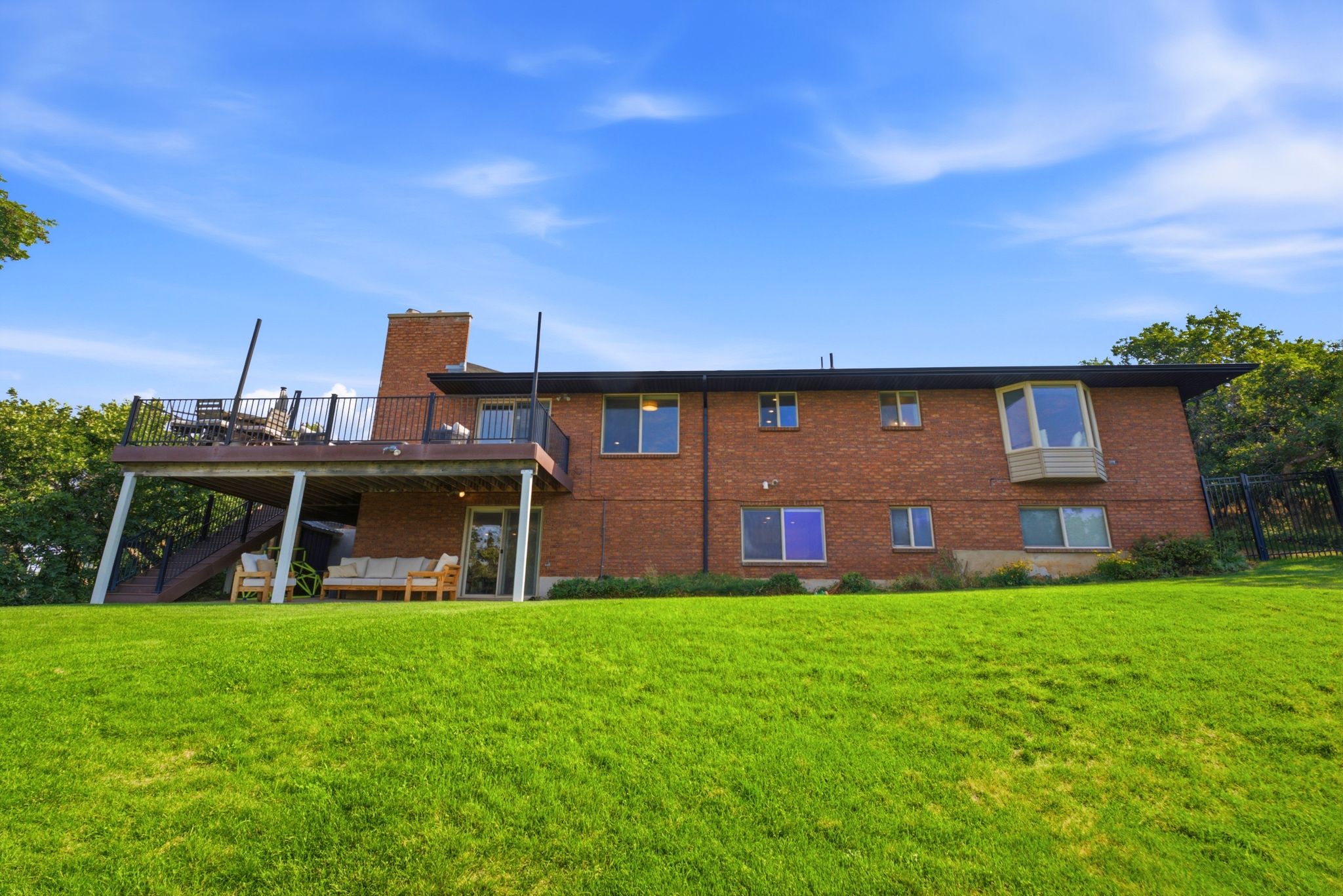 Expansive green lawn with a brick exterior featuring a multi-level deck, a prominent chimney, and a bay window