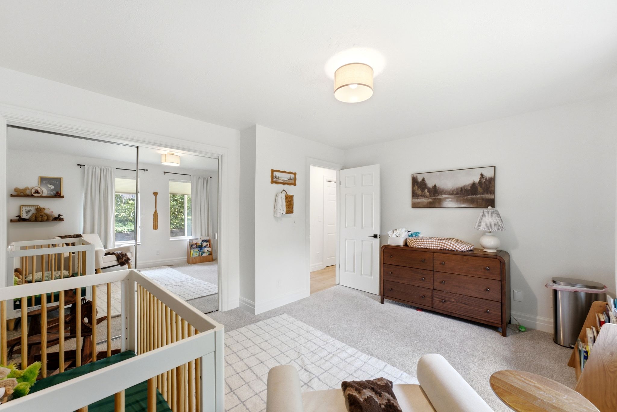 Bright room featuring white walls, light-colored carpet, a ceiling-mounted light fixture, and a white paneled door with dark hardware
