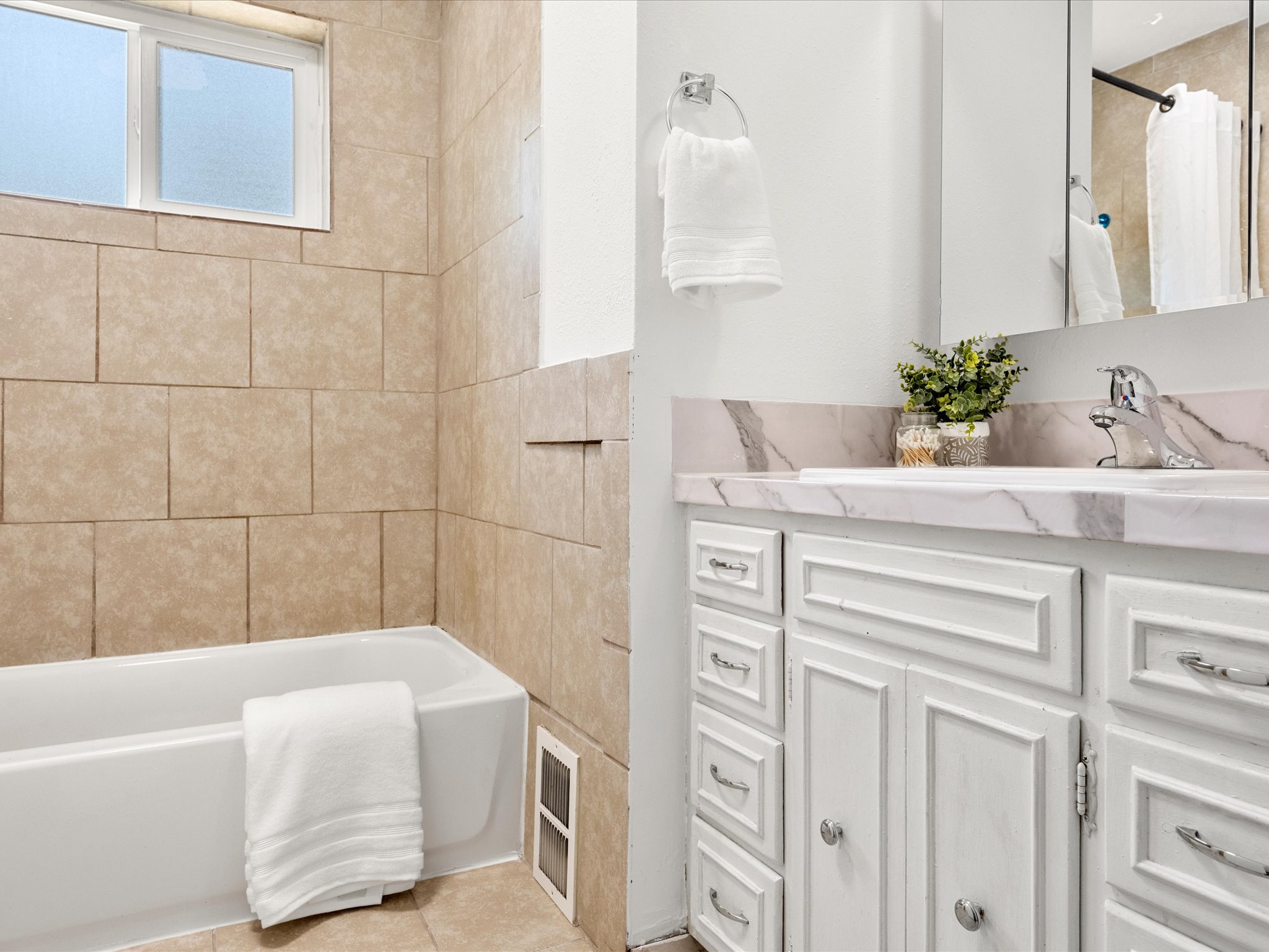 Bathroom featuring a white bathtub with light-colored tile surround, a built-in shower niche, and a frosted window