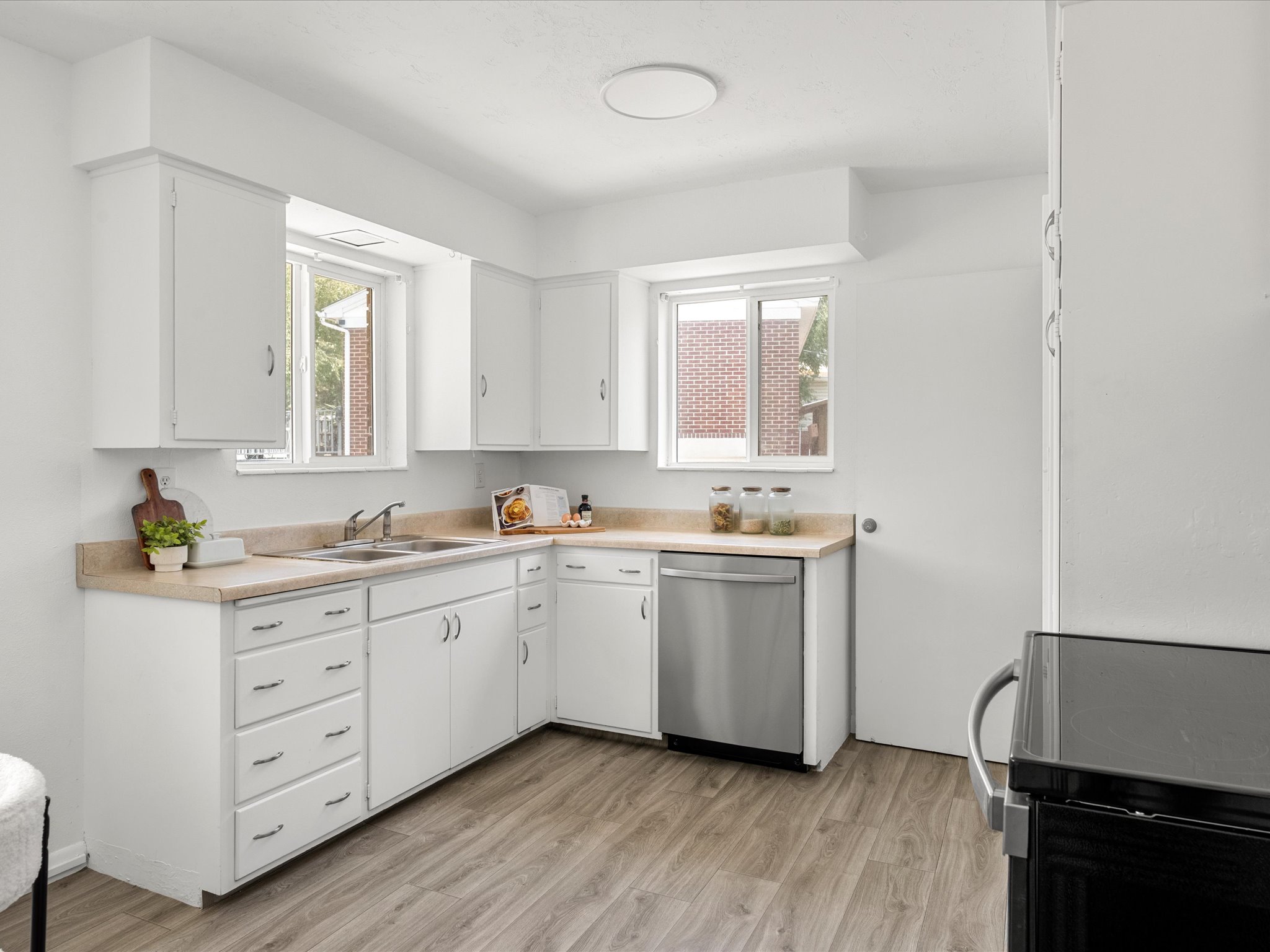Kitchen featuring white cabinetry, light-toned countertops, a stainless steel dishwasher, and wood-finish flooring