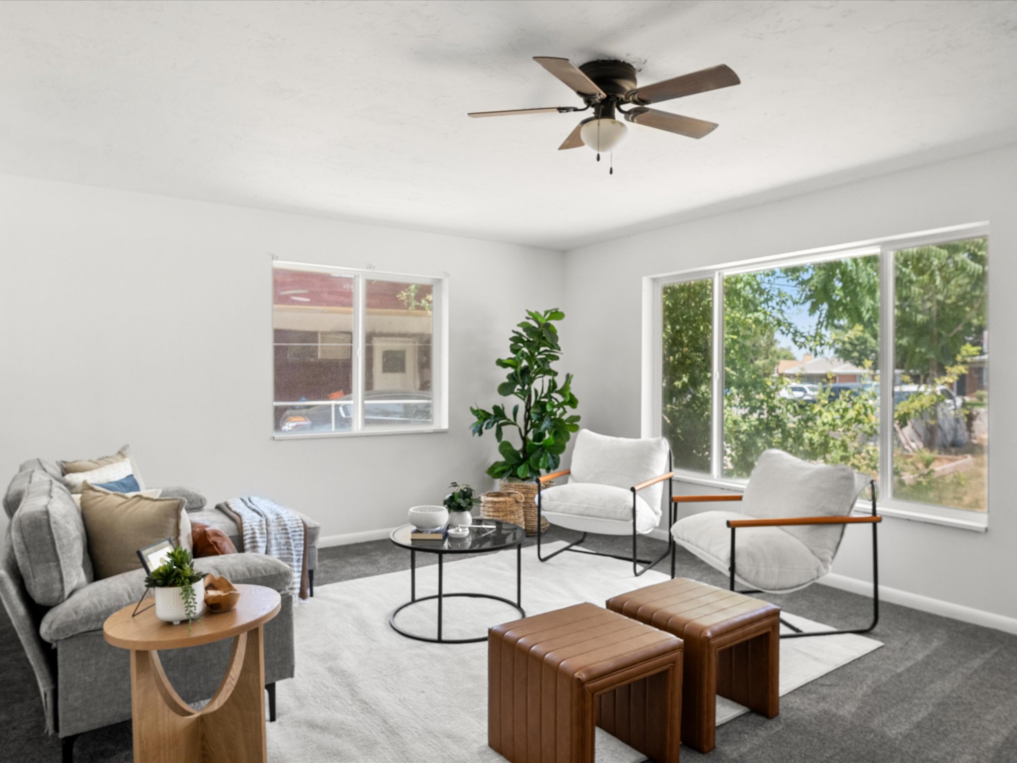 Open living space featuring a ceiling fan with light fixture, multiple windows for natural light, and soft gray carpeting