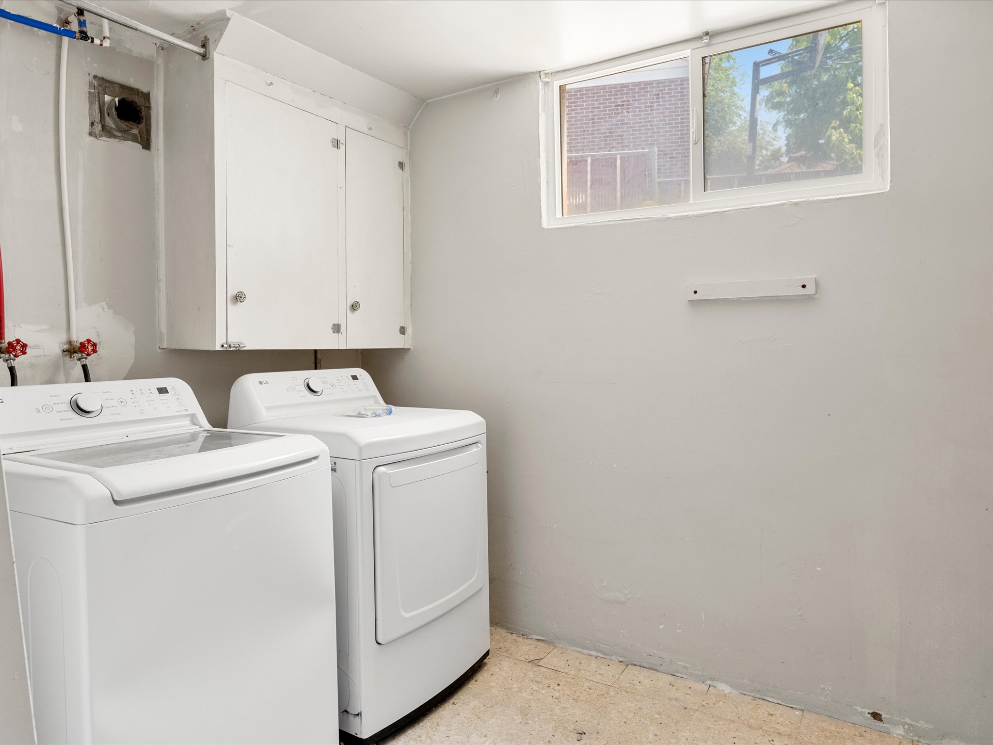 Laundry area featuring a sliding window, white upper cabinetry, and exposed plumbing