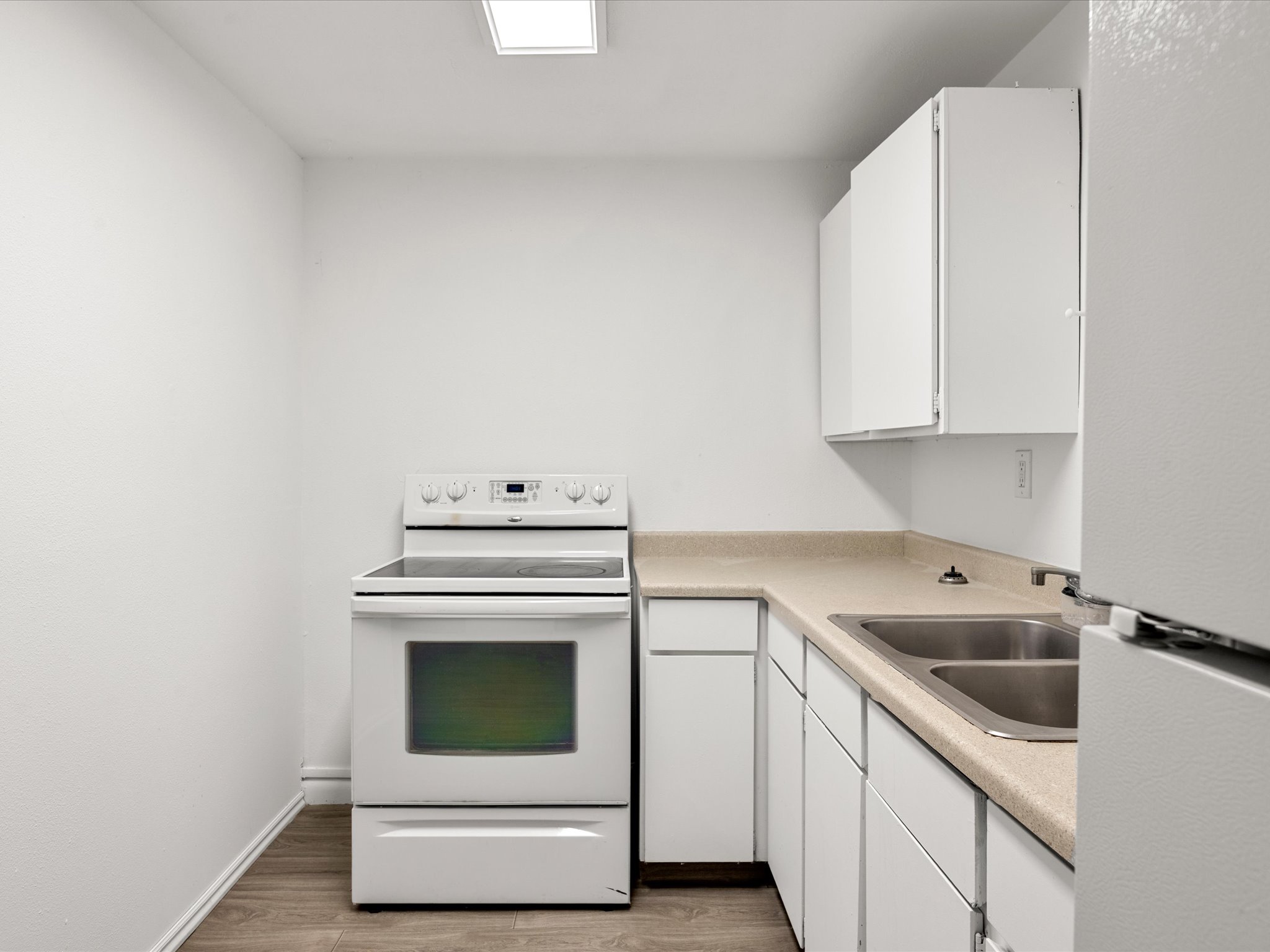 Compact kitchen featuring white cabinetry, a double basin stainless steel sink, light-toned countertops, a white electric range, and wood-finish flooring
