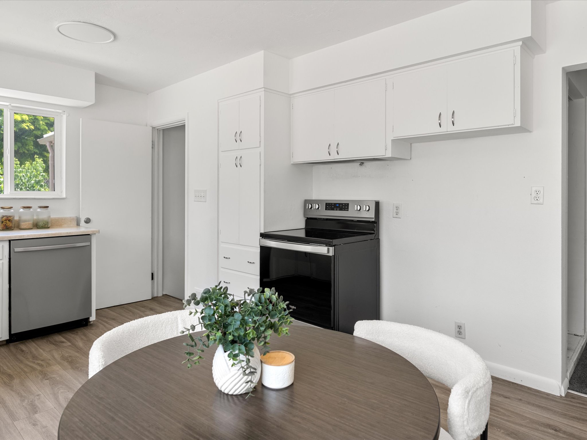 Well-appointed kitchen featuring a stainless steel dishwasher, wood-finish flooring, white cabinetry, a built-in pantry, and a contemporary black range