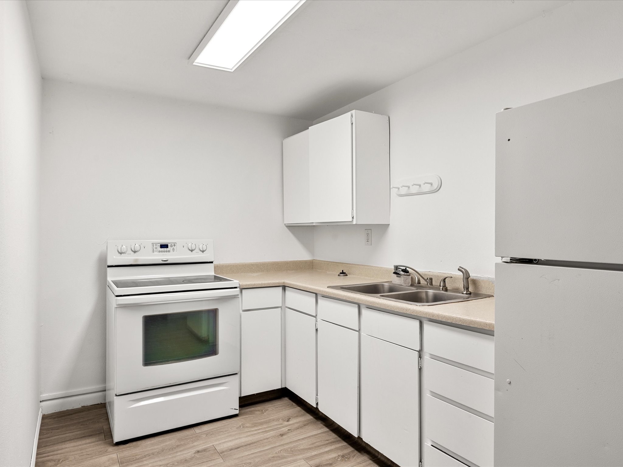 Compact kitchen featuring a white electric range, white cabinetry, laminate countertops, a double basin stainless steel sink, and wood-finish flooring