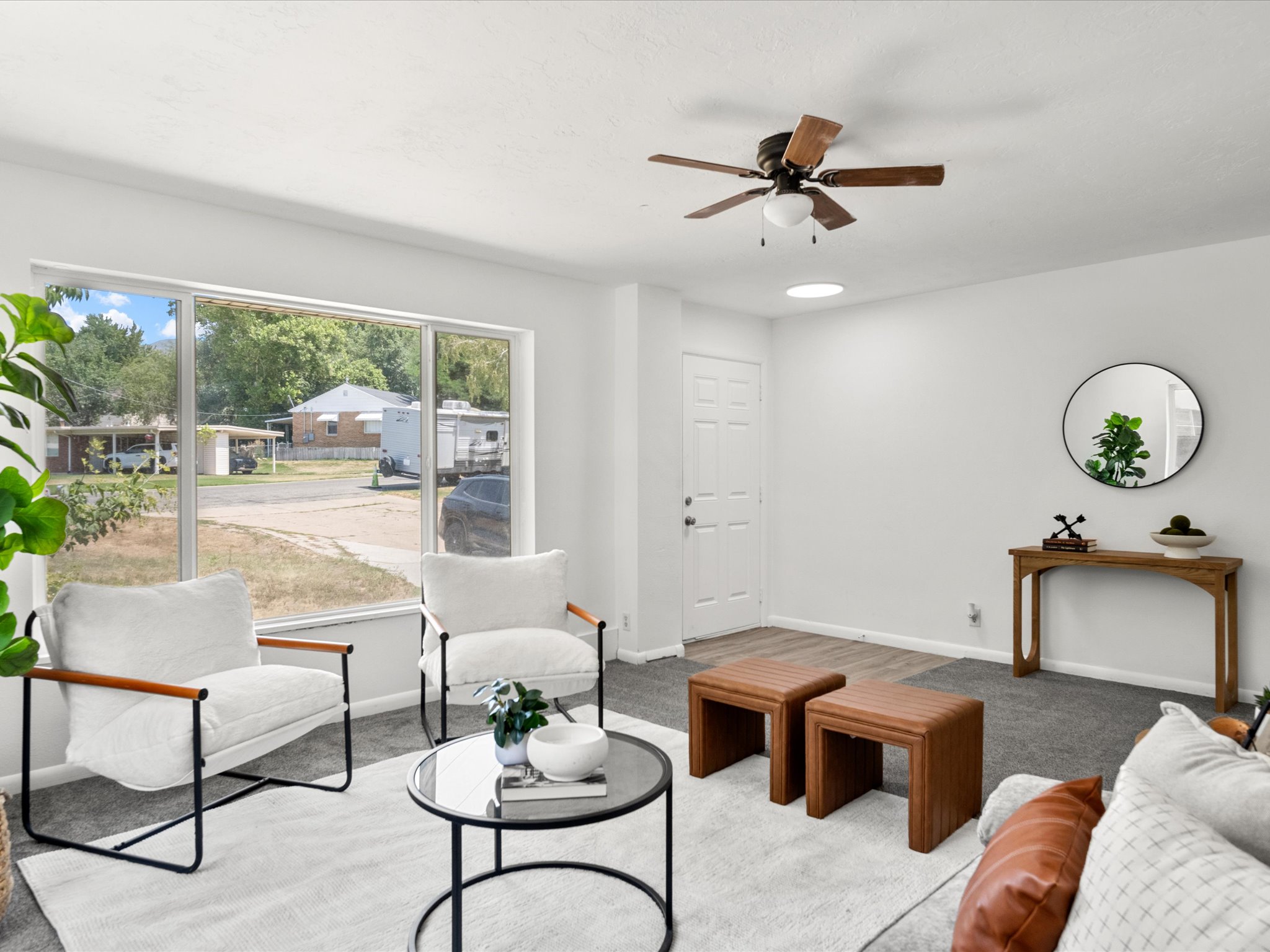 Living area featuring a large picture window, ceiling fan, and mixed flooring with carpet and wood-finish sections