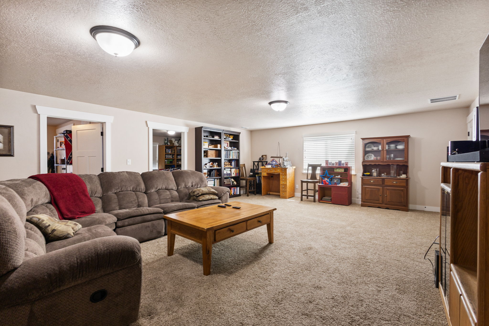 Spacious carpeted room featuring multiple doorways with white trim, a large window with blinds, and recessed lighting