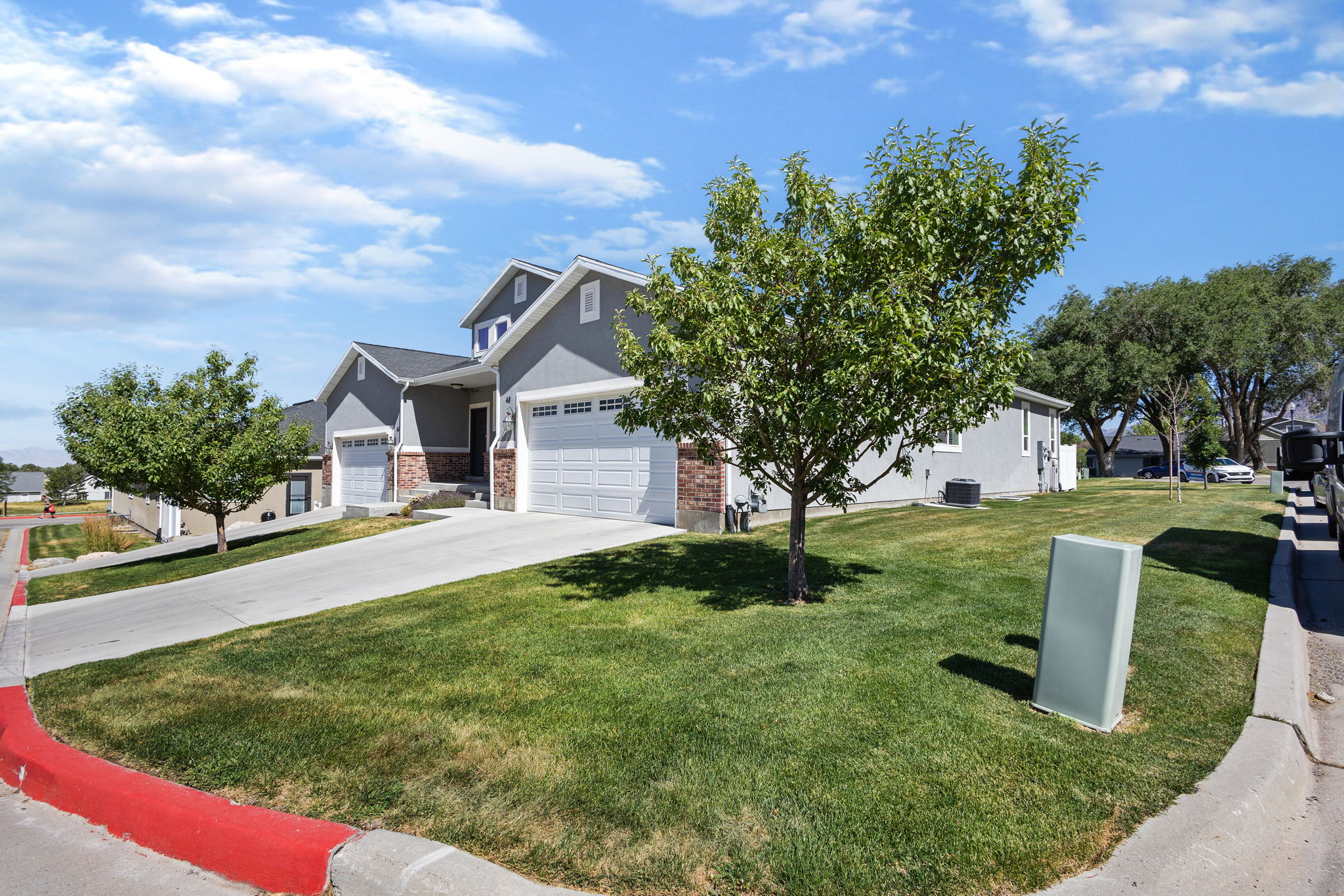 Contemporary duplex exterior featuring gray siding, stone veneer accents, and white garage doors