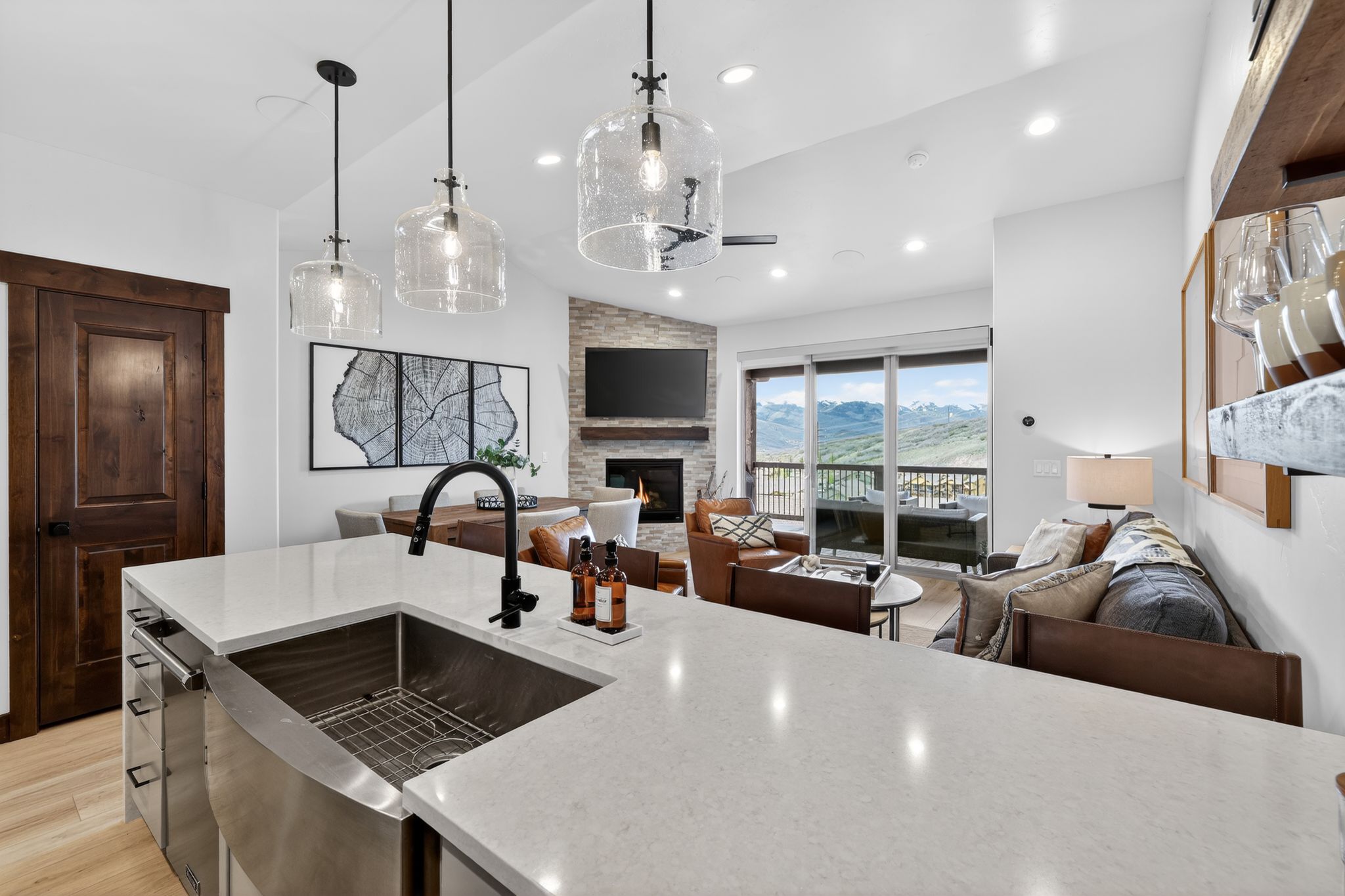 Open-concept kitchen featuring an apron-front stainless steel sink, quartz countertops, and three clear glass pendant lights