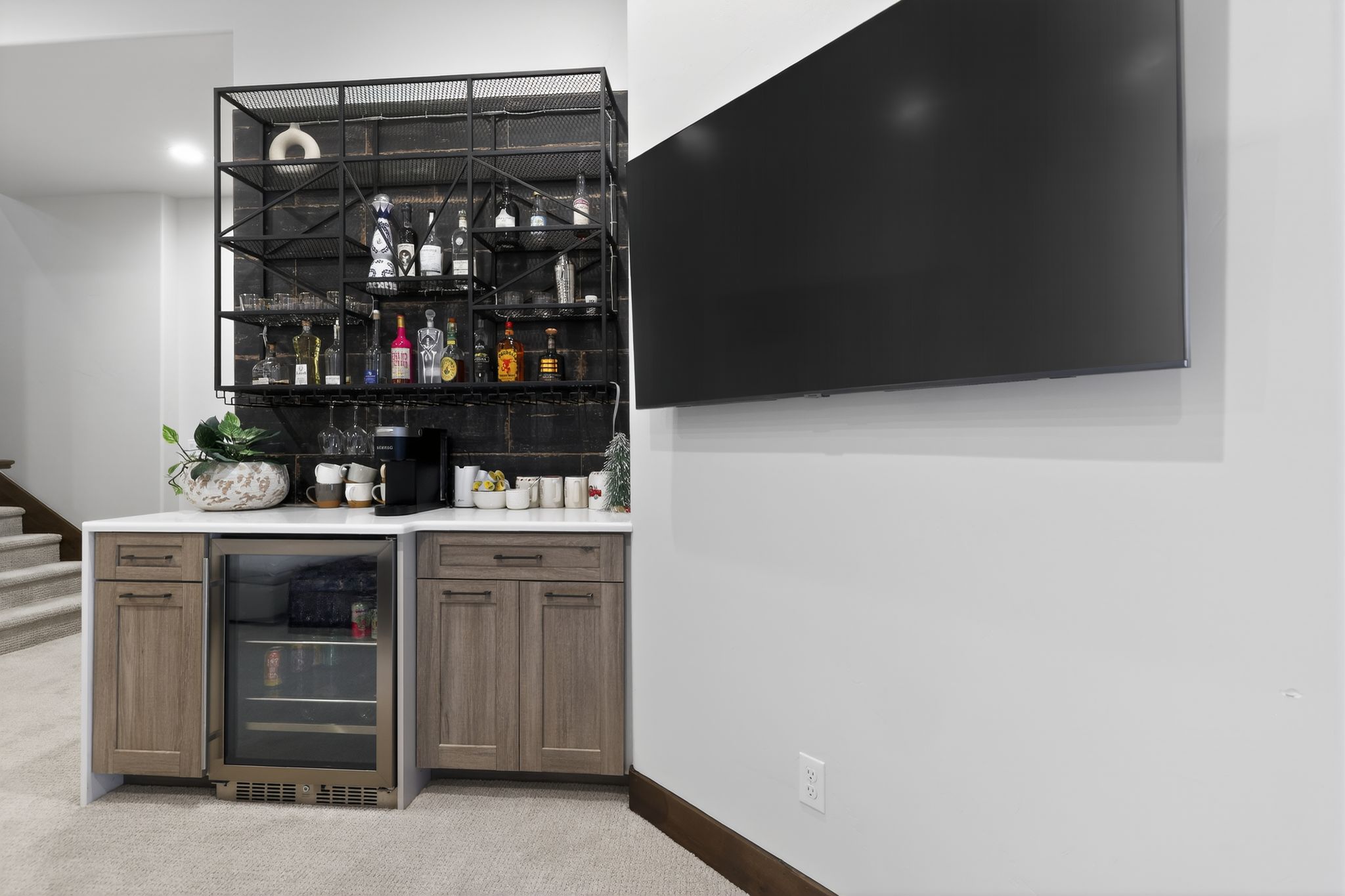 Built-in wet bar featuring a beverage refrigerator, light-toned cabinetry, and a dark metal open shelving system