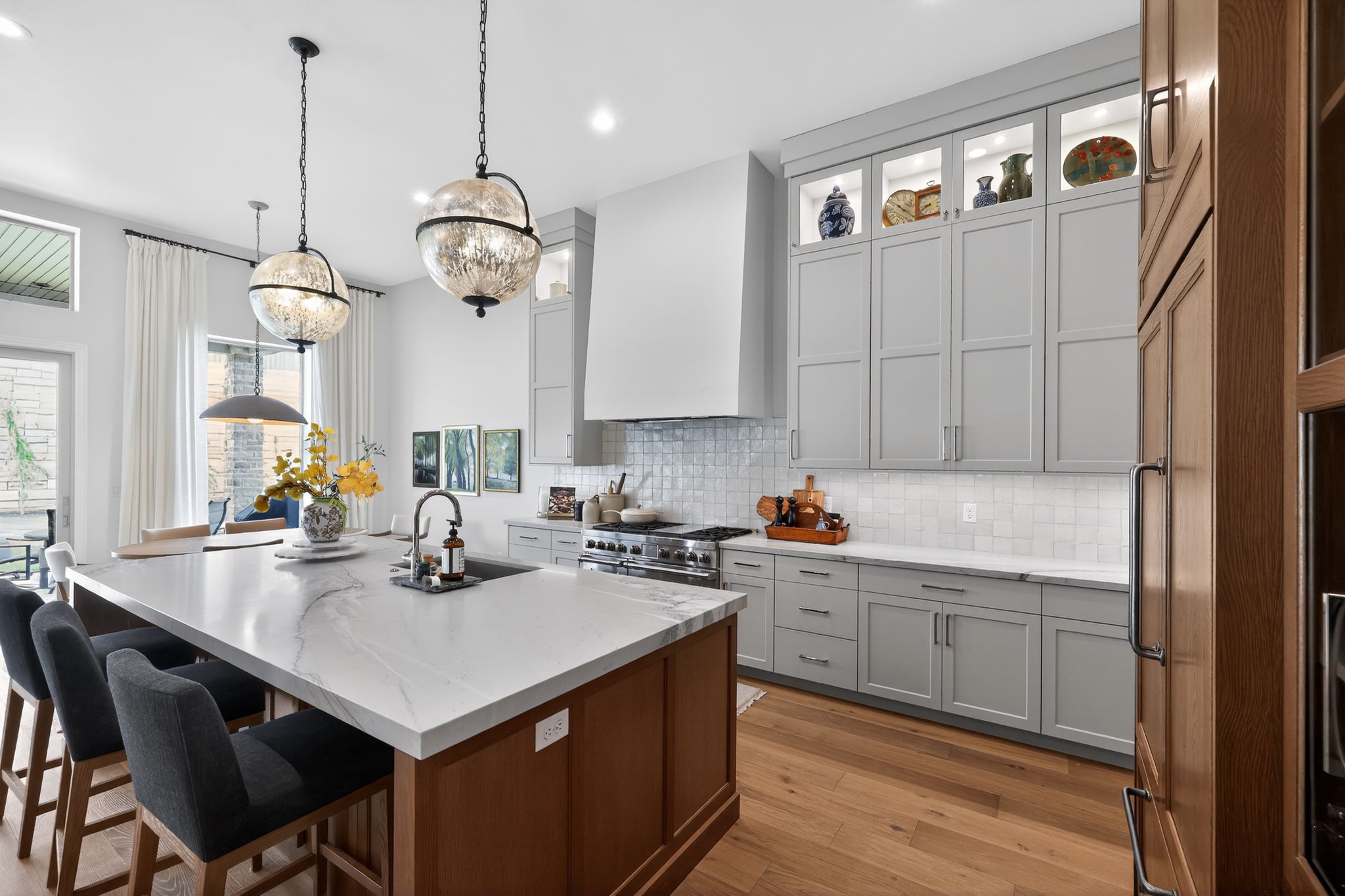 Gourmet kitchen featuring a substantial central island with seating, a professional-grade range, custom cabinetry with integrated lighting, a tile backsplash, and wood-finish flooring