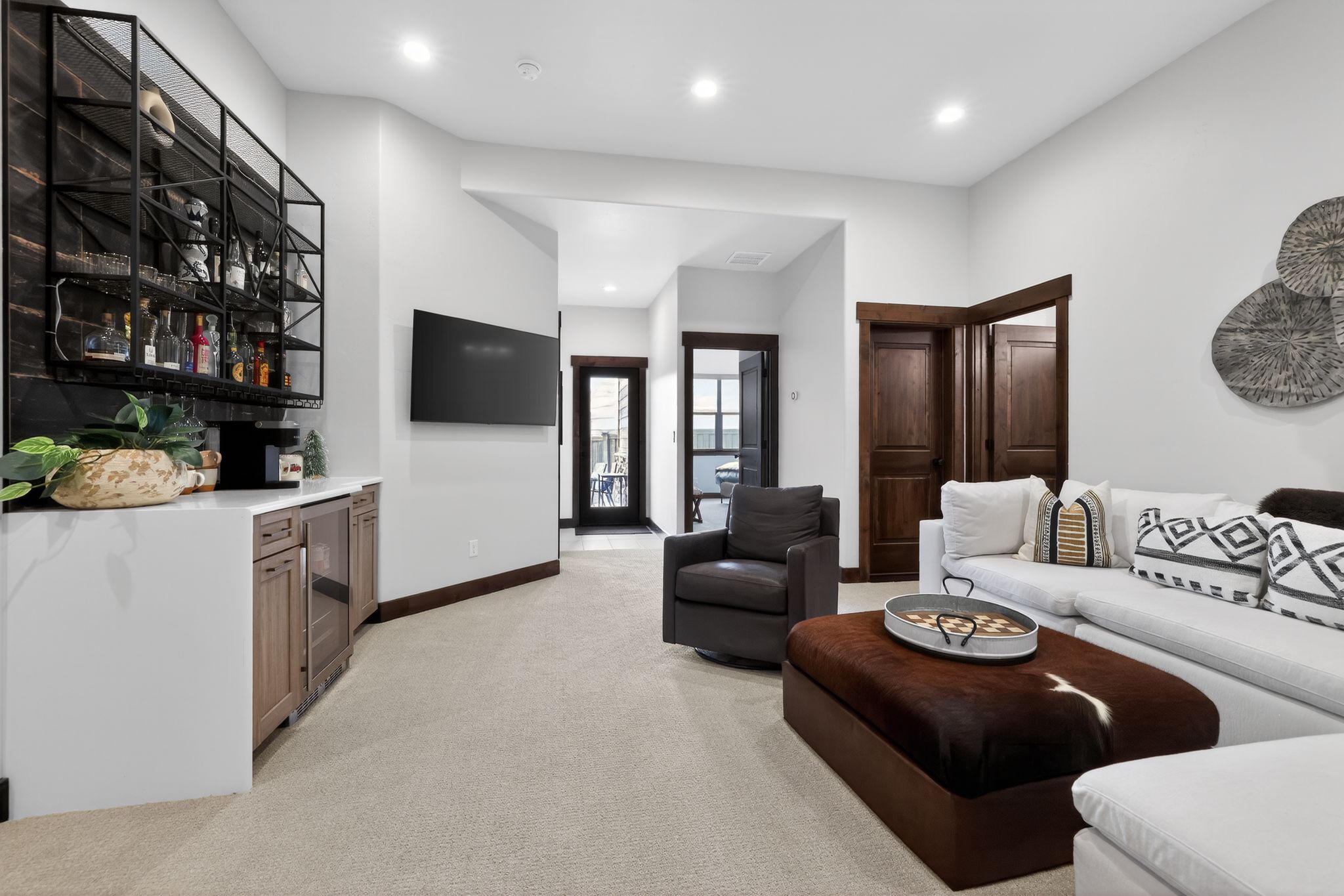 Carpeted recreation room featuring a built-in wet bar with cabinetry, floating shelving, and a beverage refrigerator