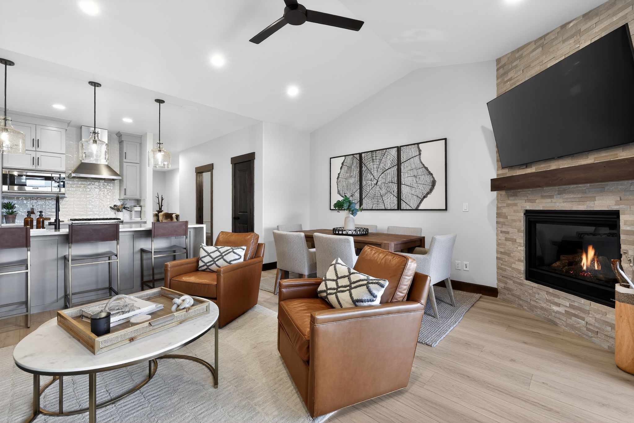 Open-concept living space featuring a stacked stone fireplace with a wood mantel, vaulted ceilings, and light wood-finish flooring