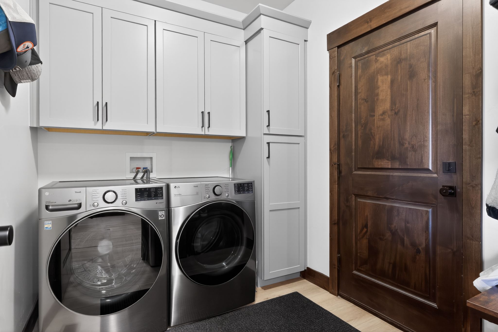Laundry area featuring light gray shaker-style cabinetry with matte black hardware, wood-finish flooring, and a dark wood door with matching trim