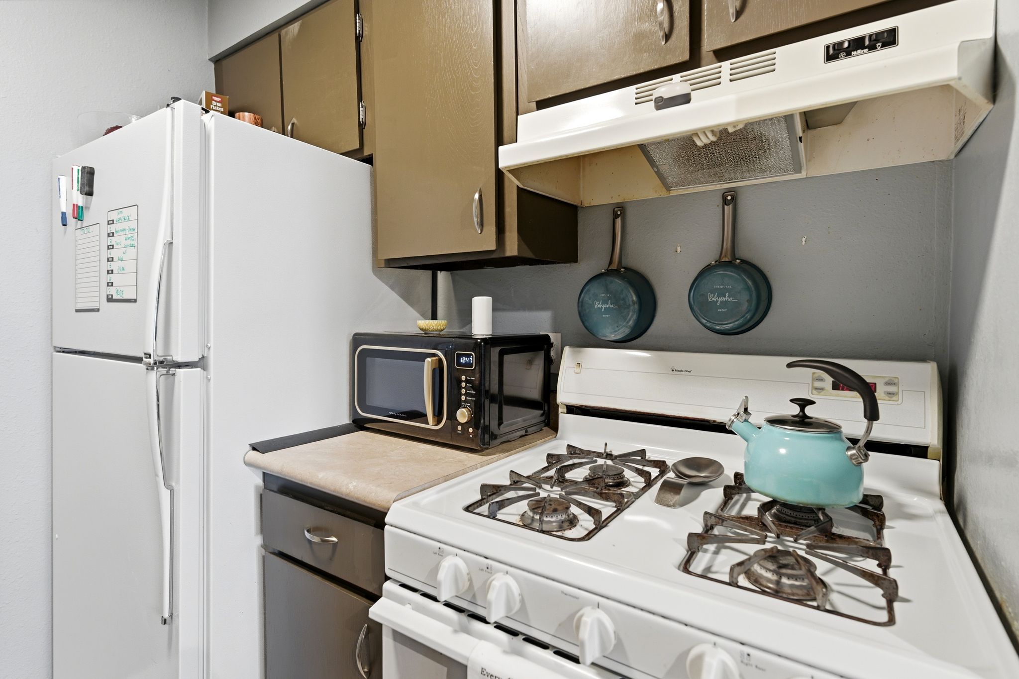 Compact kitchen featuring a white refrigerator, gas range, and range hood