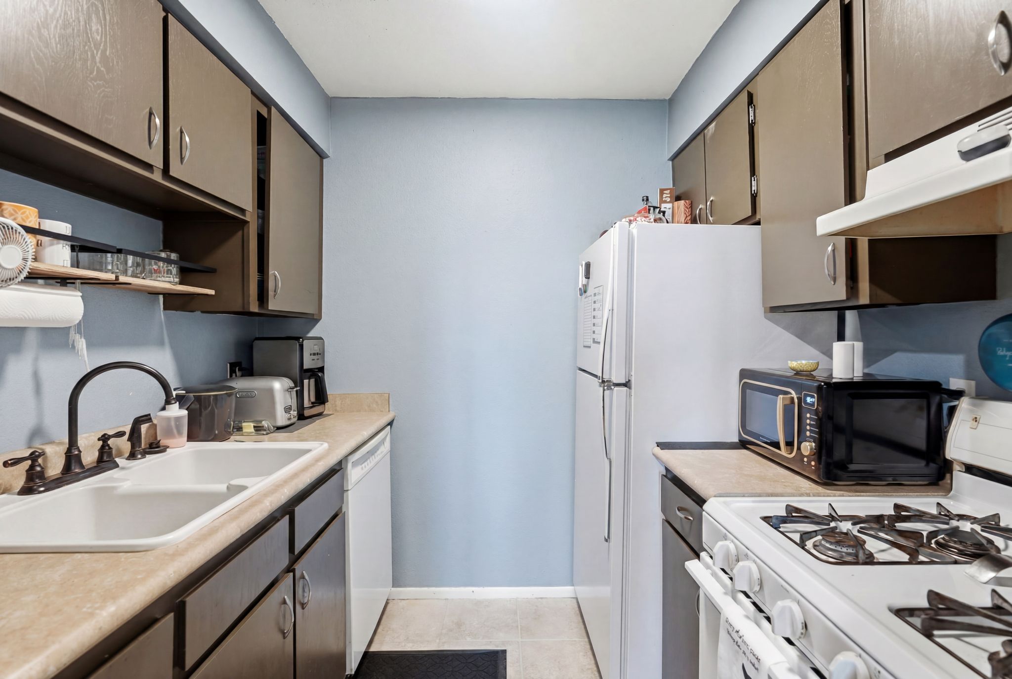 Galley kitchen featuring a dual-basin sink with a dark bronze faucet, ample cabinetry, and light-toned countertops
