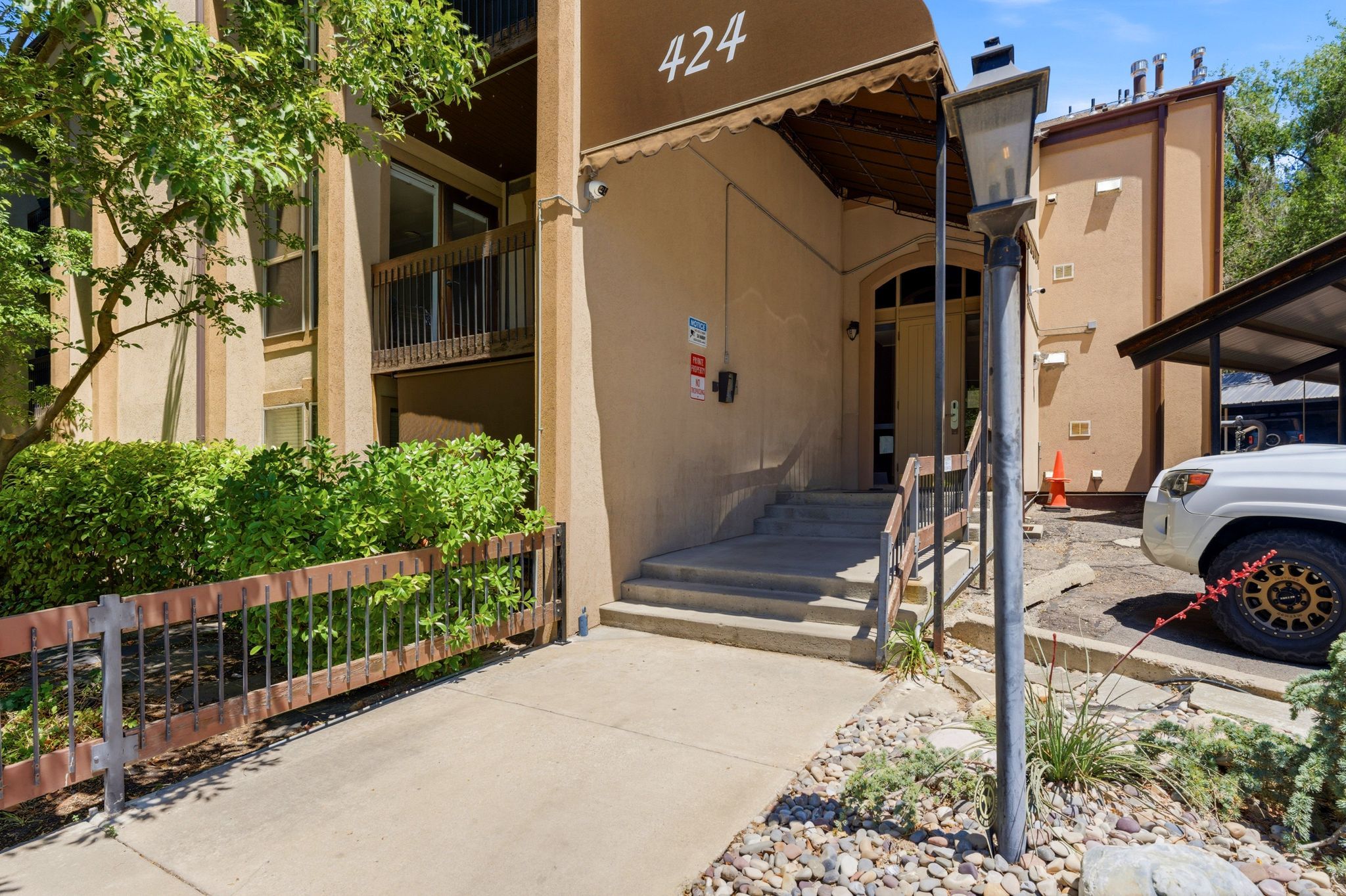 Exterior building entrance featuring a brown awning, concrete steps with handrails, and a prominent street lamp
