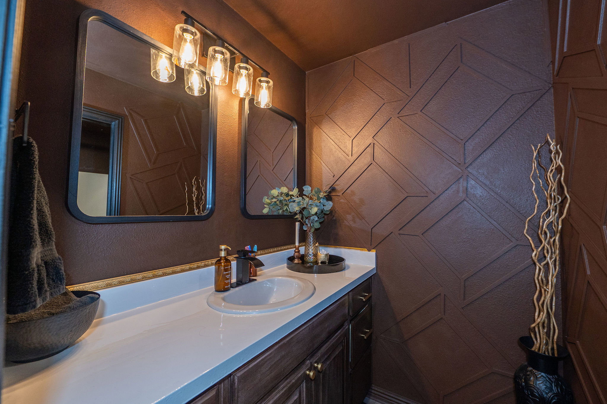 Bathroom vanity featuring a single basin sink, white countertop, and dark wood-finish cabinetry with brass hardware