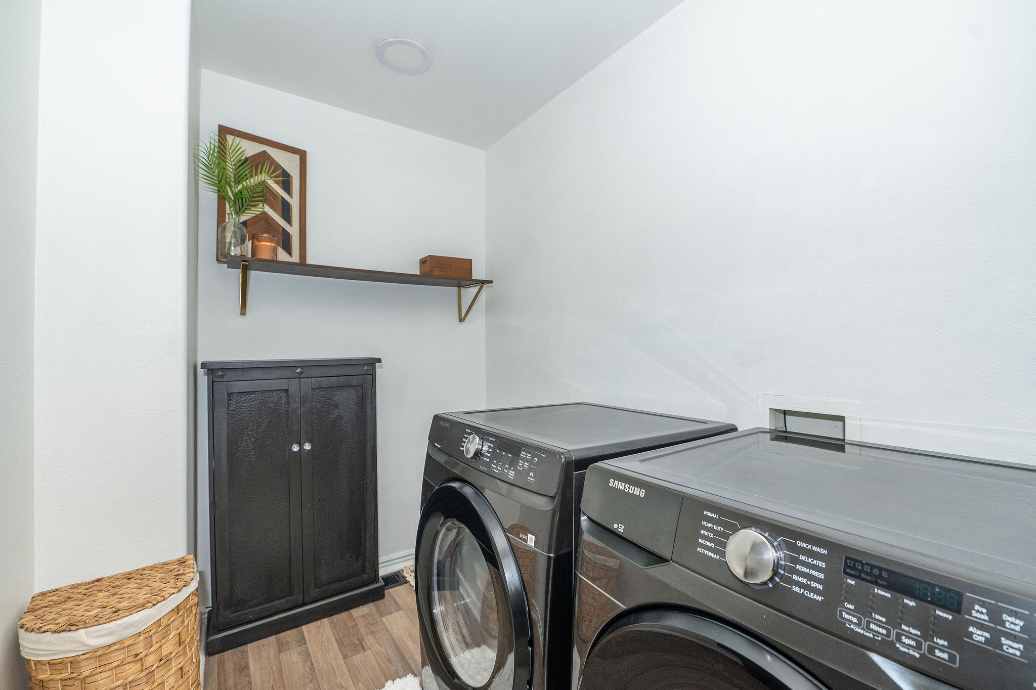 Dedicated laundry space featuring wood-finish flooring and a built-in dark wood storage cabinet