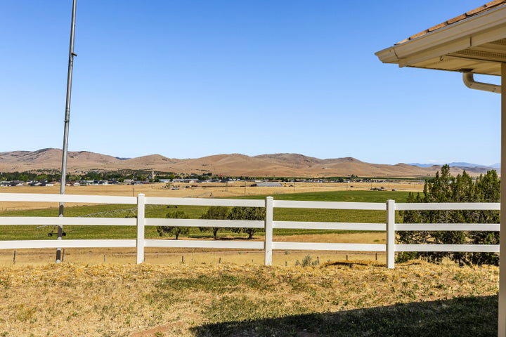 Expansive rural landscape featuring a white three-rail fence, distant mountains, and green fields