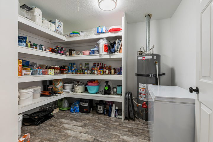 Utility room featuring extensive built-in shelving, wood-finish flooring, a water heater, and a white chest freezer