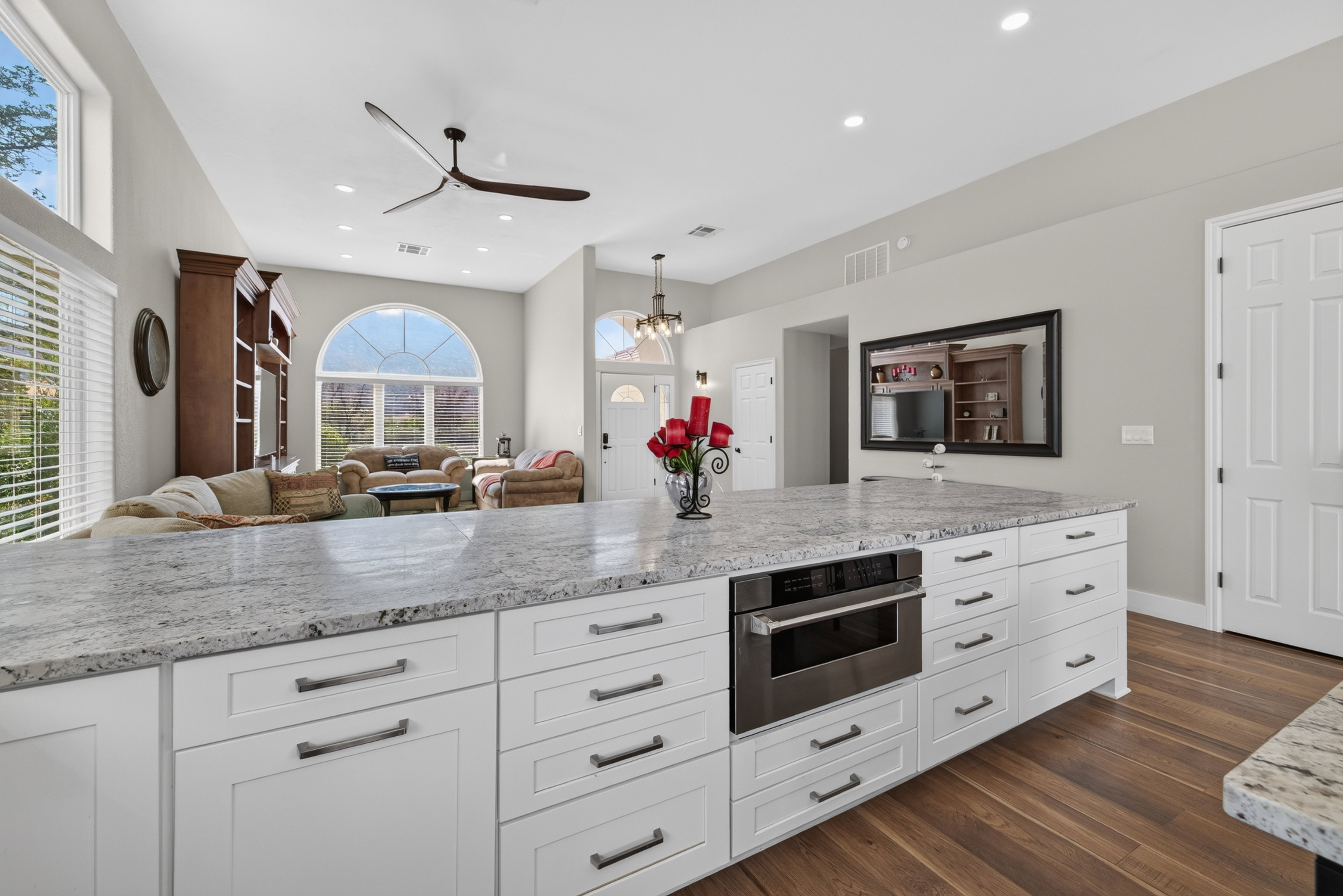 Spacious kitchen island featuring stone-finish countertops, white cabinetry with dark pulls, and a built-in stainless steel microwave drawer