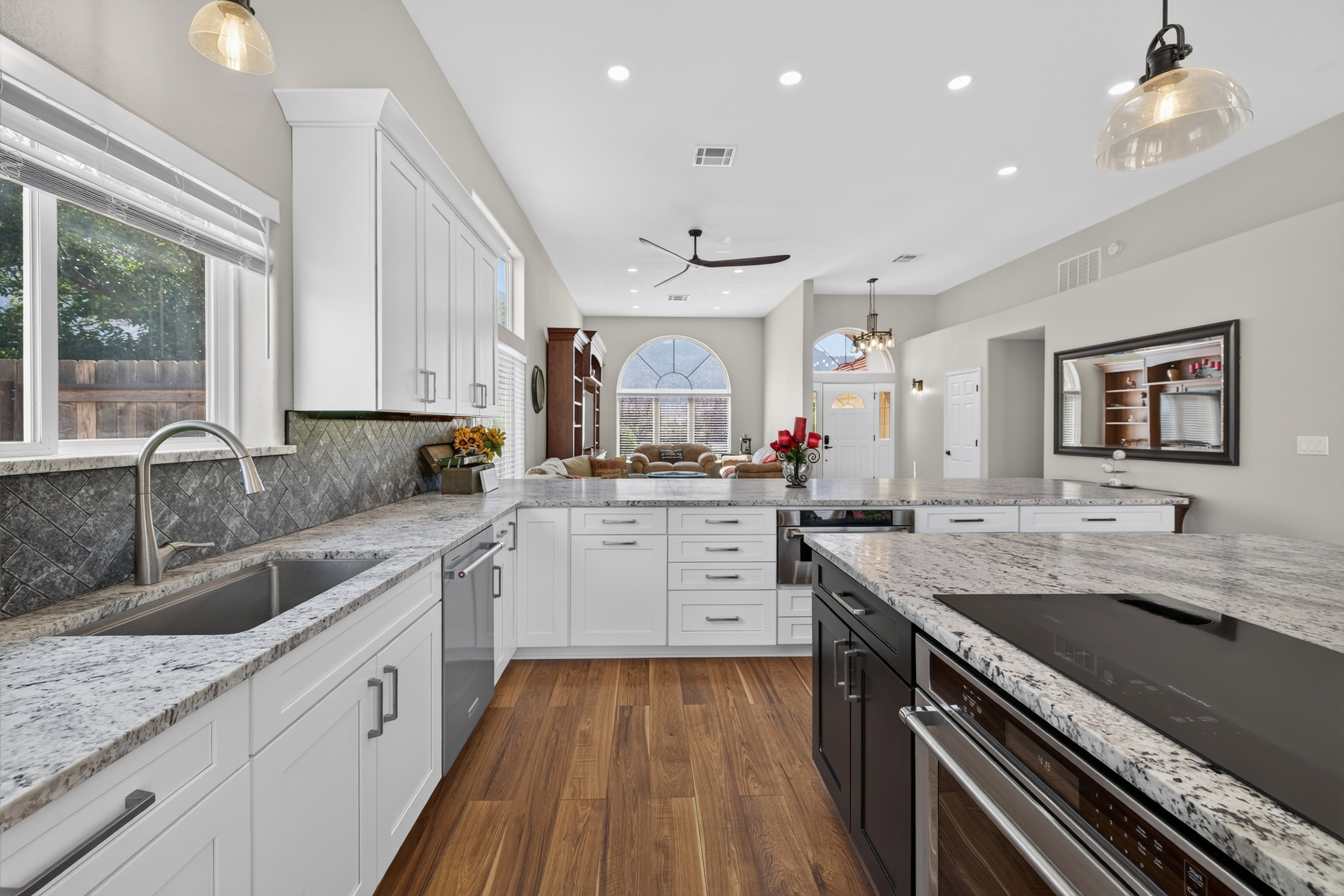 Modern kitchen featuring white cabinetry, light granite countertops, stainless steel appliances, wood-finish flooring, and a dark herringbone pattern backsplash