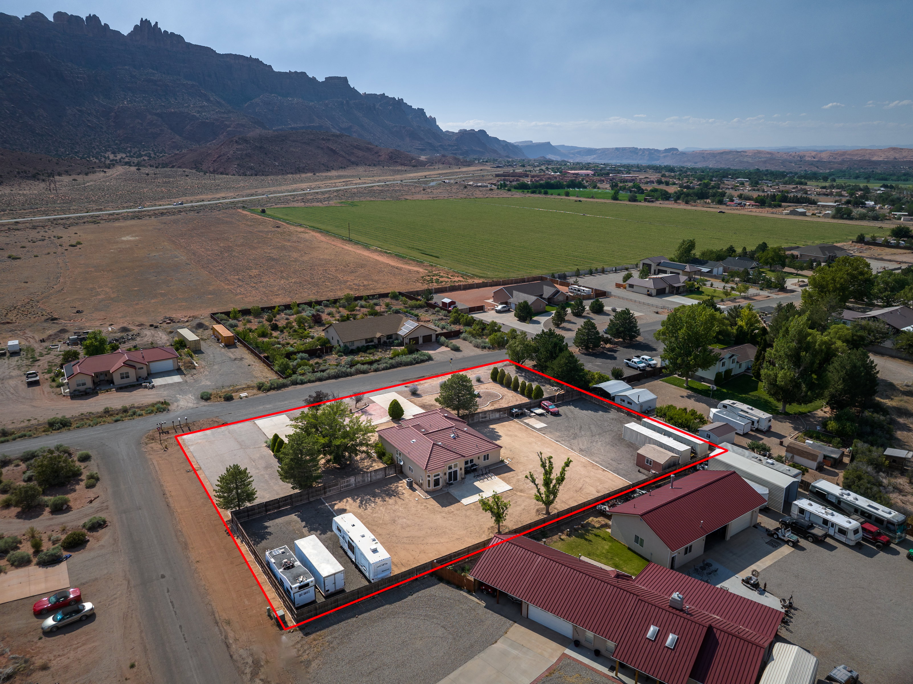 Expansive property featuring a main residence with a red tile roof, an additional outbuilding with a red metal roof, and a large paved area for multiple vehicles