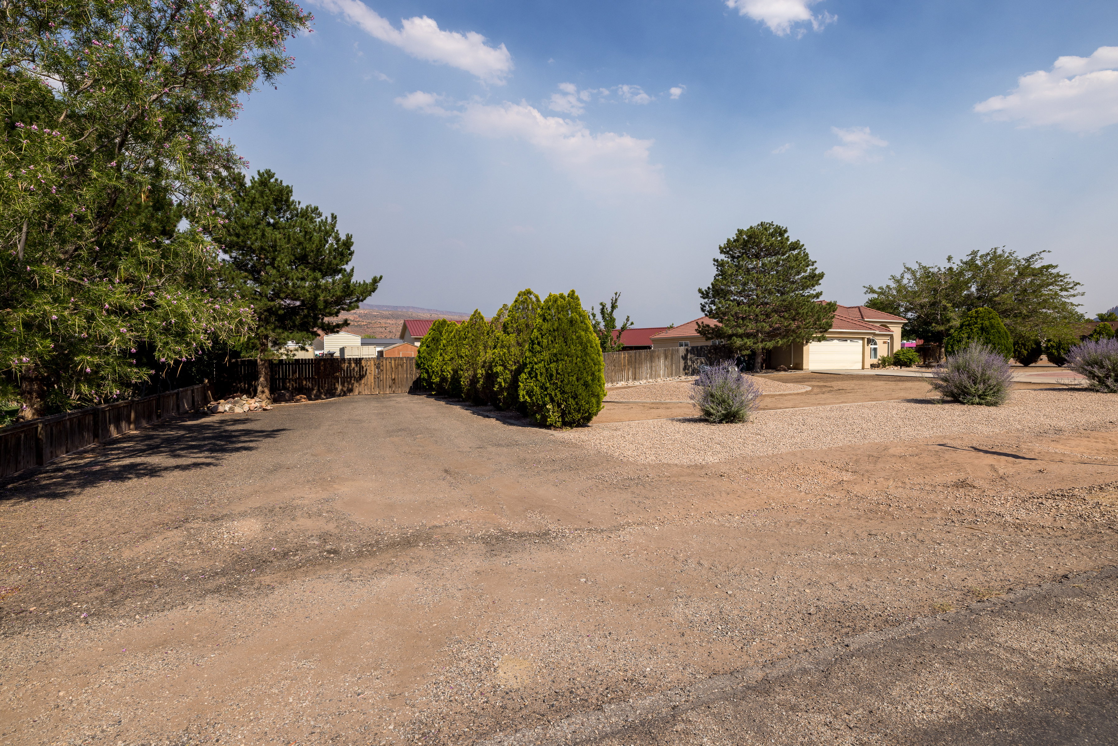 Expansive gravel driveway bordered by mature trees and shrubs, offering privacy