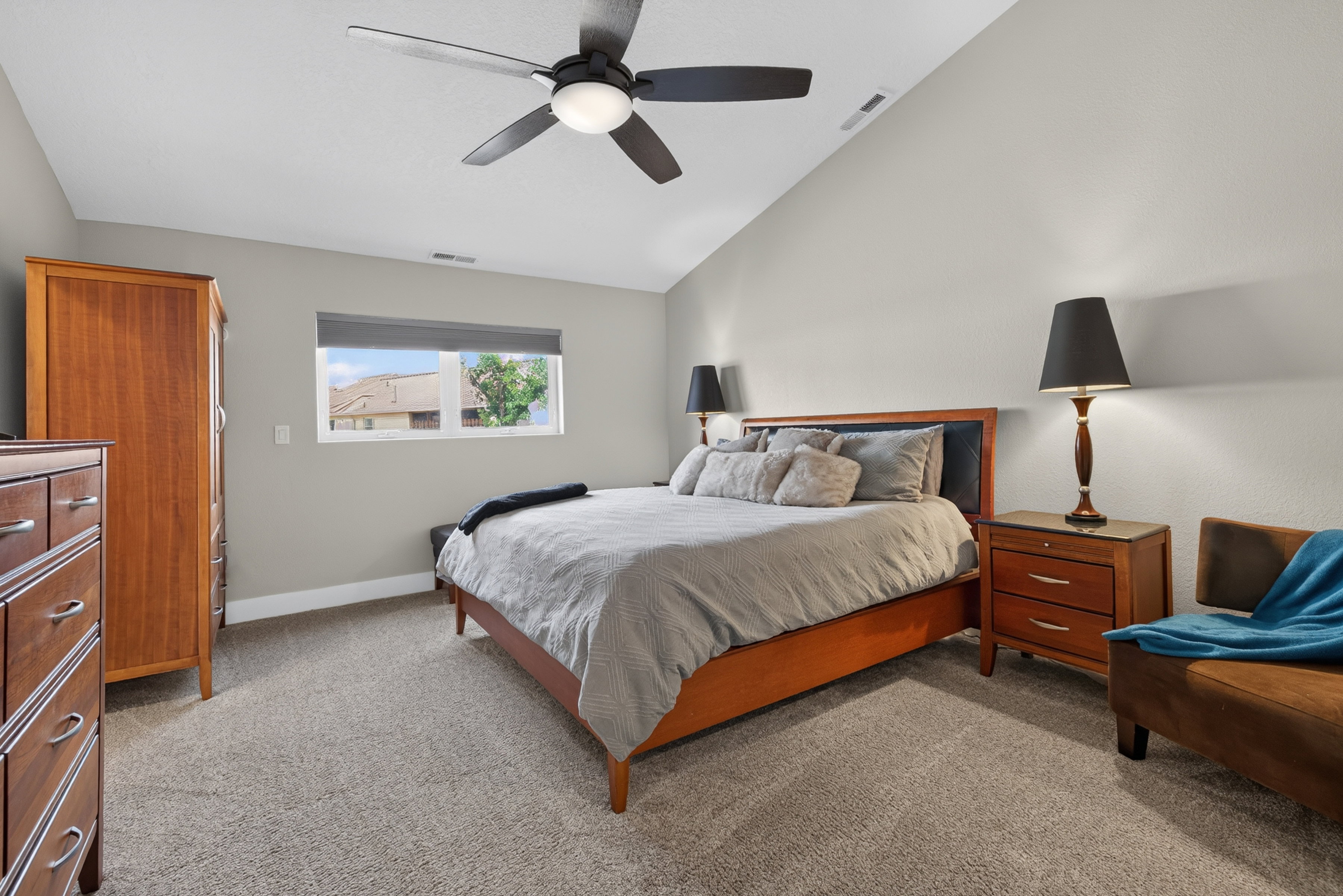 Spacious room featuring vaulted ceilings, a contemporary ceiling fan with integrated lighting, window with roller shade, and plush carpeting