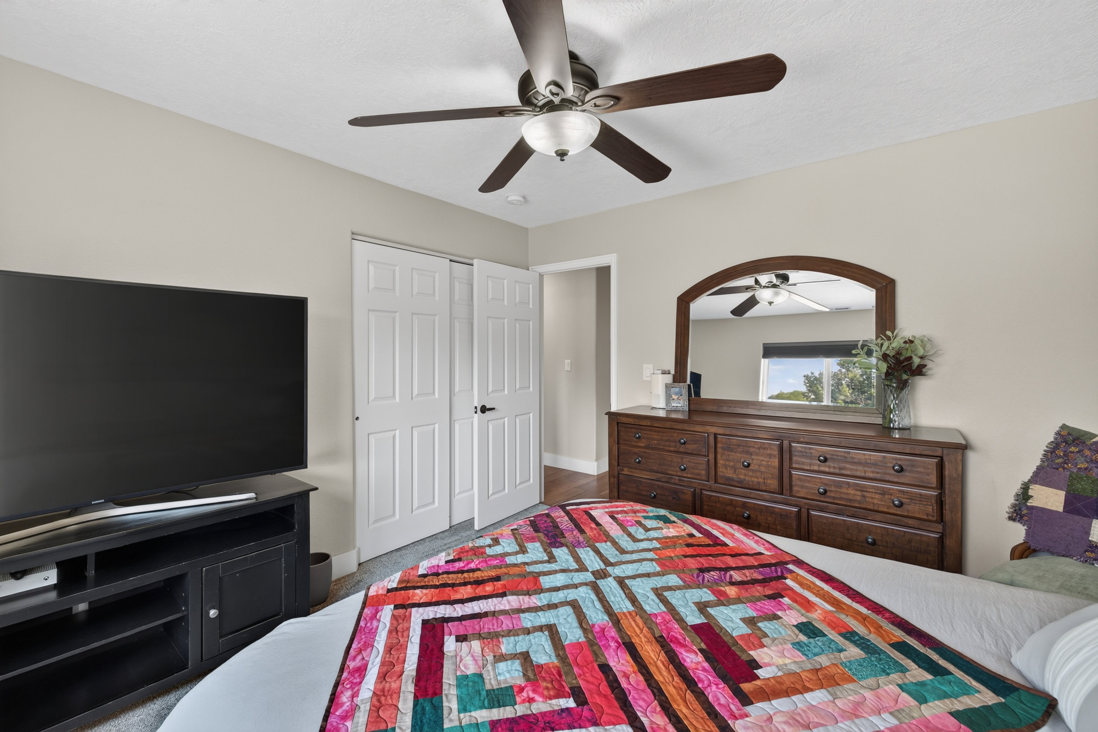Neutral-toned interior featuring a ceiling fan with integrated lighting, wood-finish flooring, and white paneled bi-fold doors
