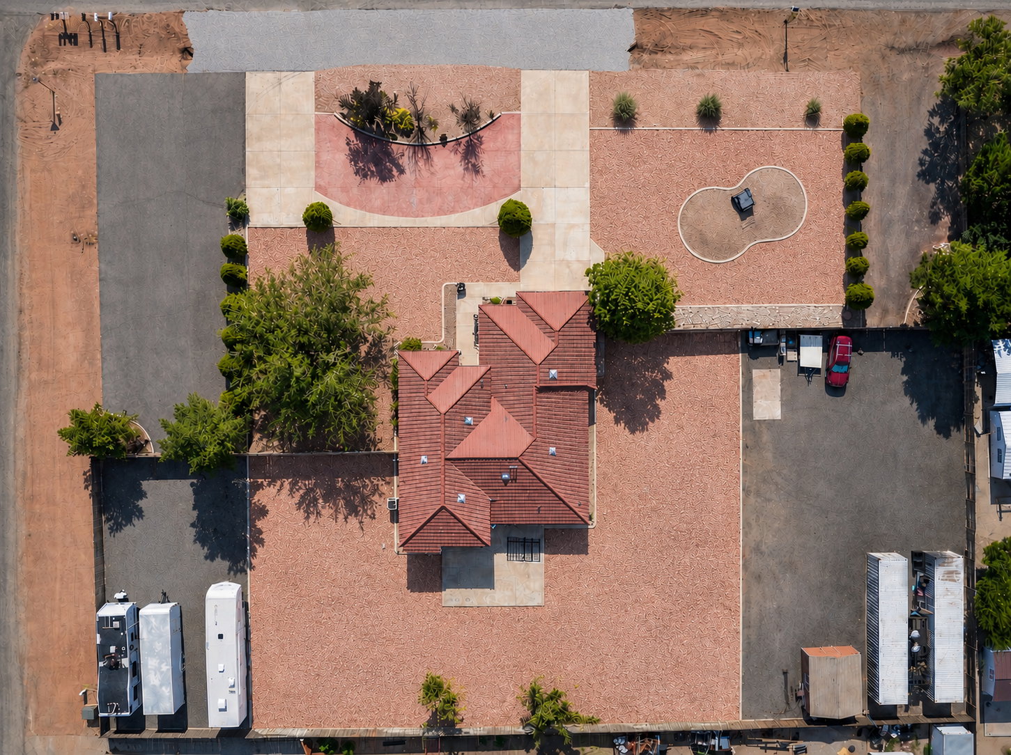 Expansive property featuring a central building with a terracotta-style tiled roof, extensive gravel landscaping, multiple paved parking areas, and mature trees. AI generated to show options of landscaping