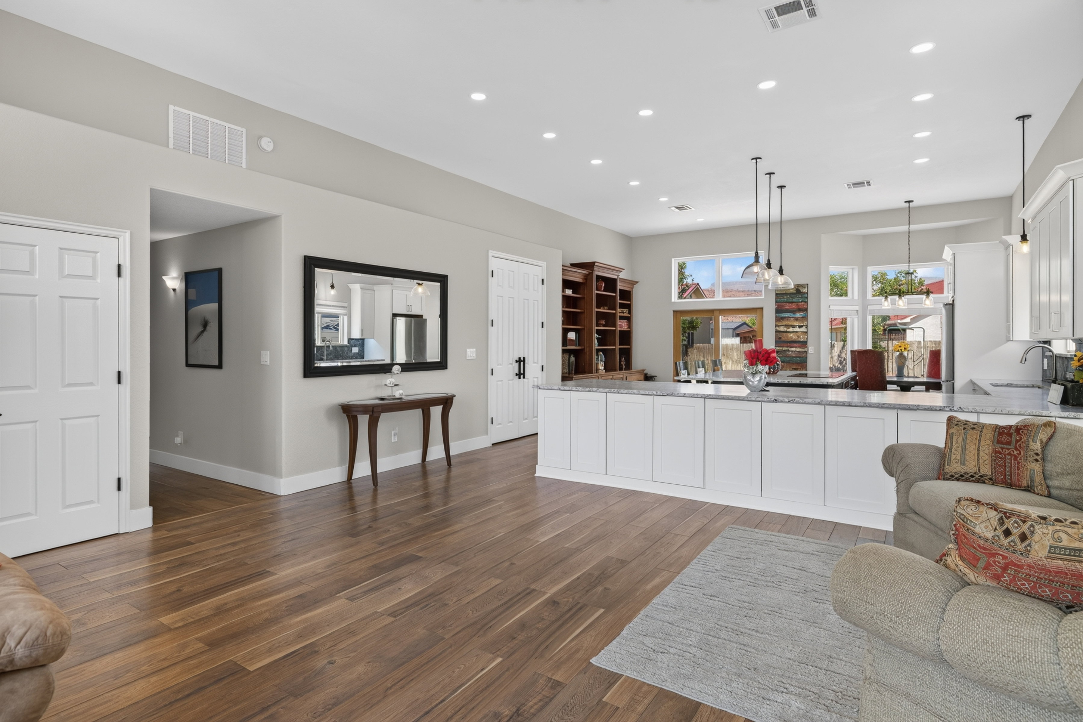 Open-concept kitchen and living area featuring wood-finish flooring, recessed lighting, white cabinetry, and granite countertops