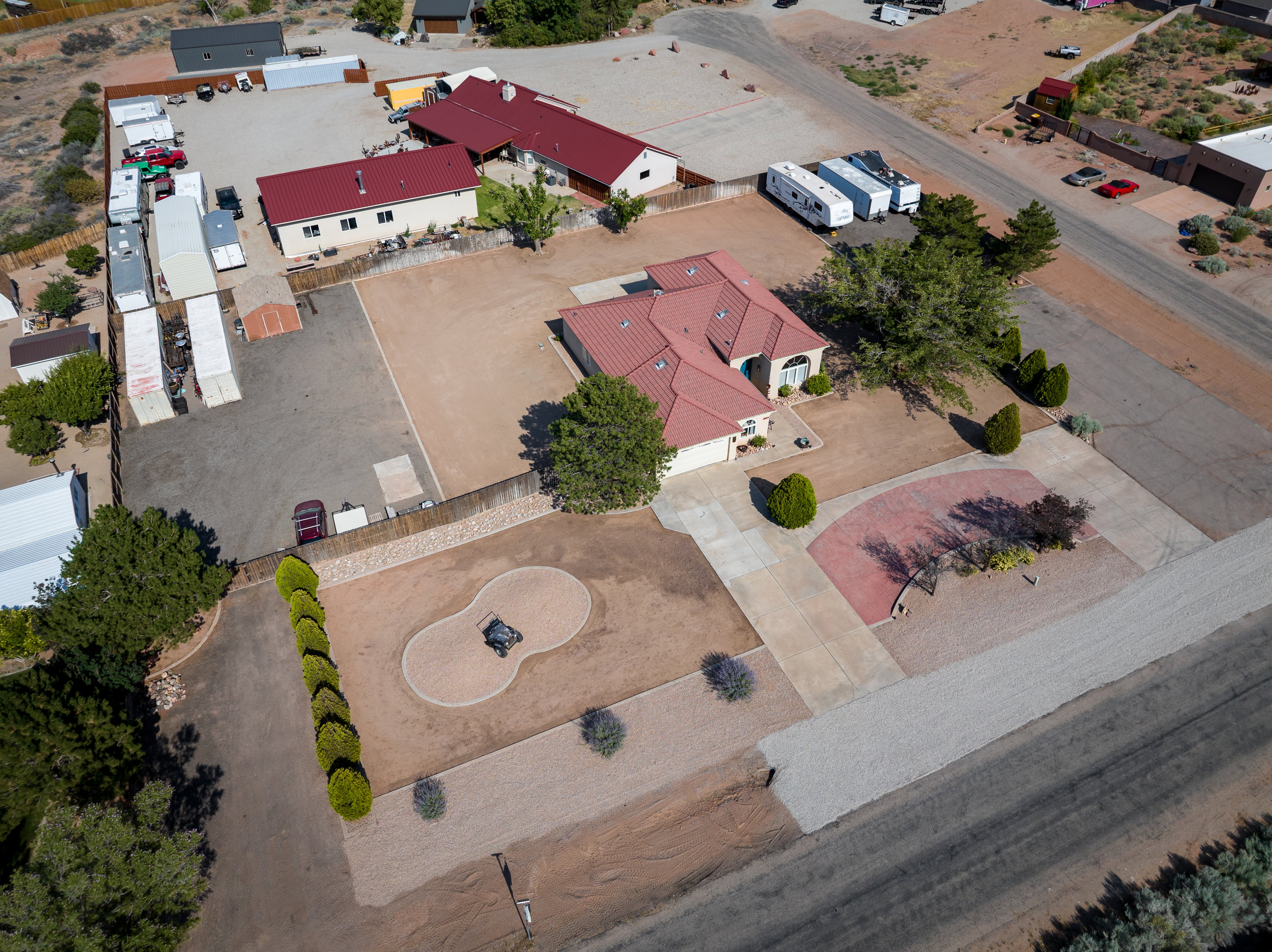 Extensive property featuring a primary residence with a red tile roof, a large unpaved lot with storage units, a secondary building with a red tile roof, and a paved driveway with a brick paver accent