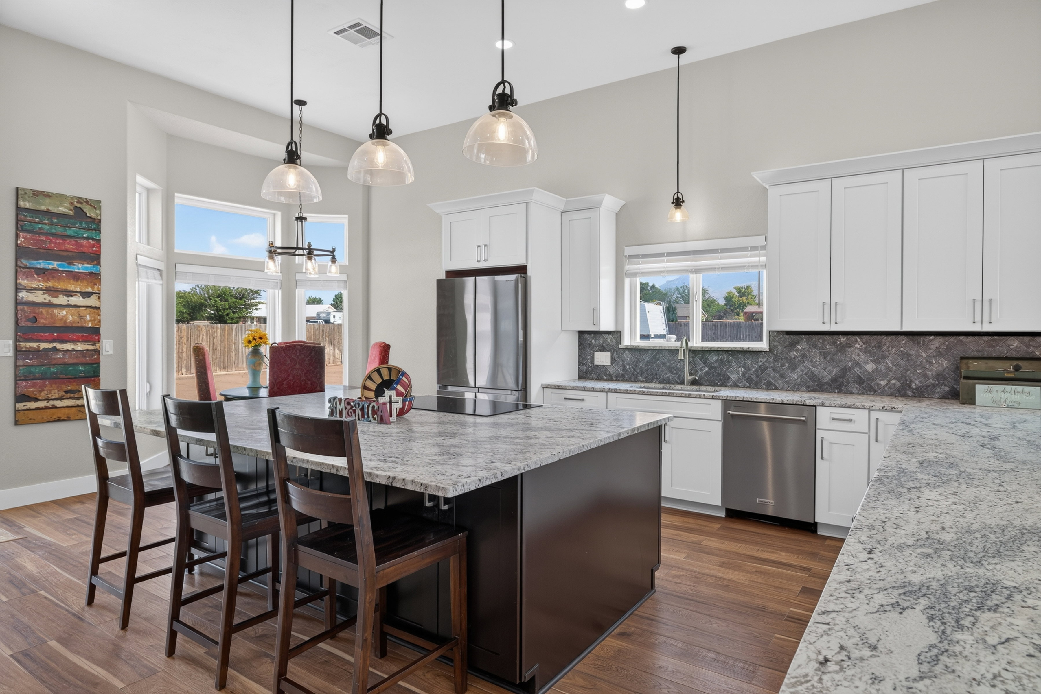 Contemporary kitchen featuring an expansive center island with seating, stainless steel appliances, white cabinetry, and wood-finish flooring