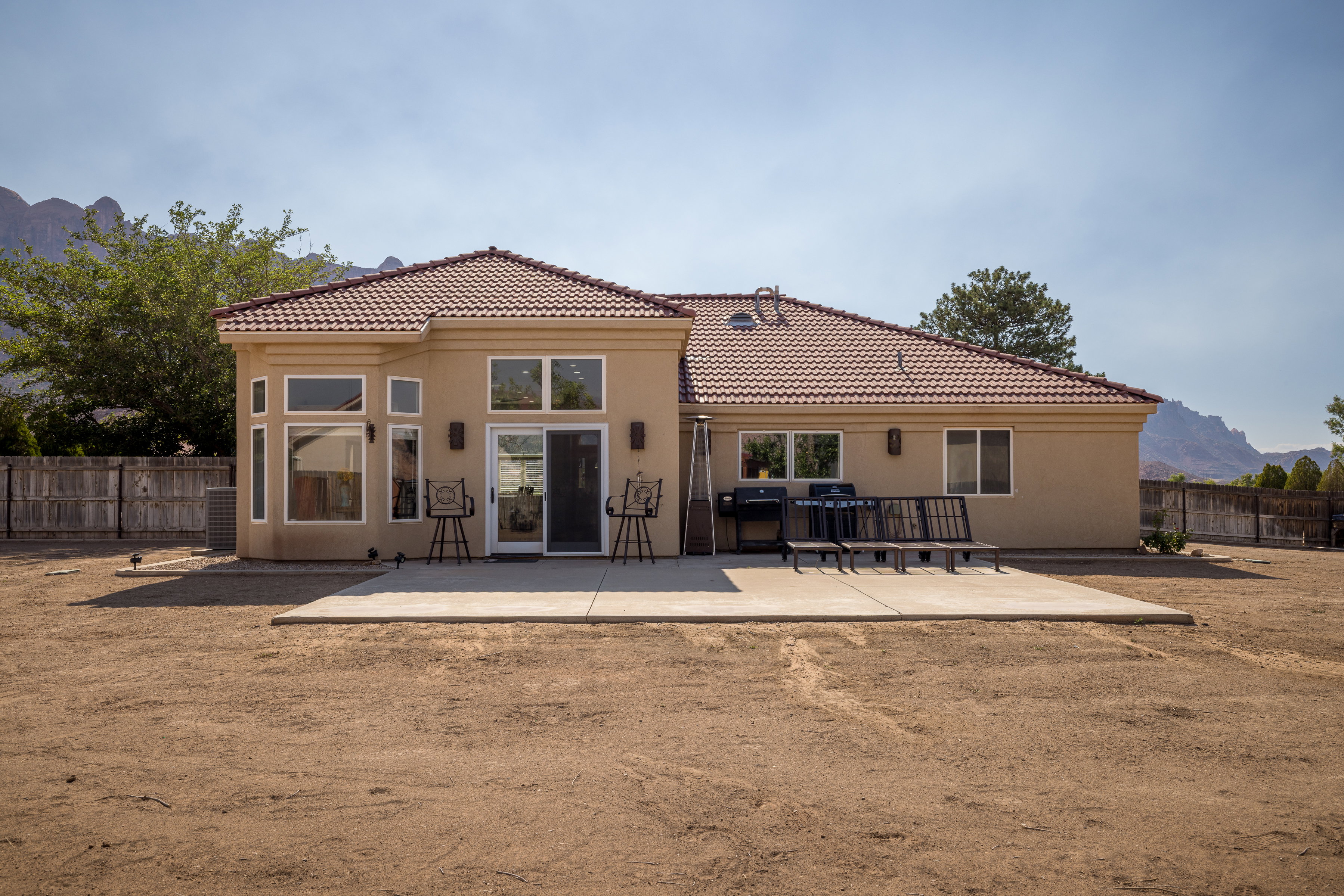Rear exterior featuring a tile roof, stucco finish, expansive concrete patio, multiple windows, and a sliding glass door