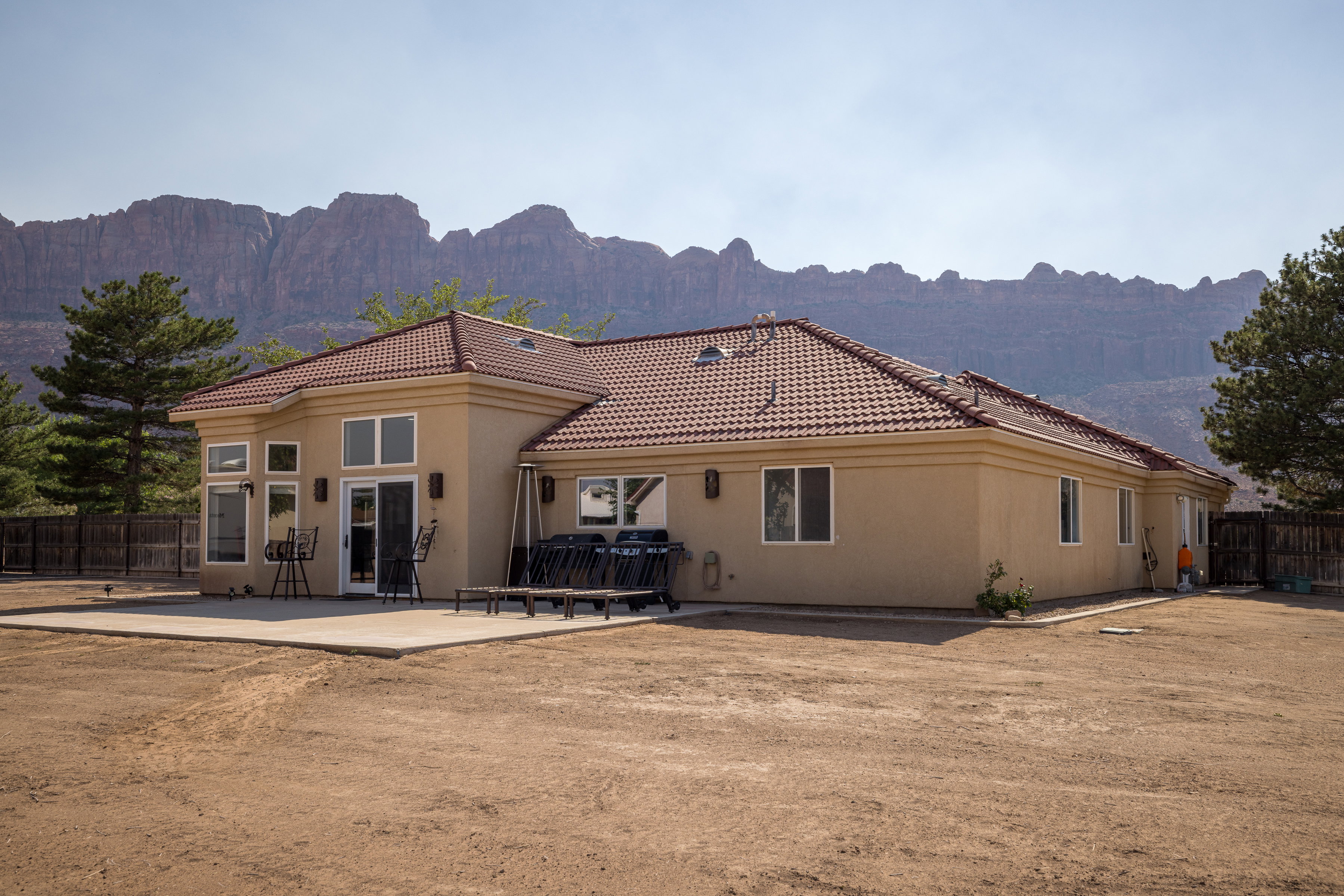 Stucco exterior featuring a red tile roof, multiple windows, a sliding glass door, and a concrete patio