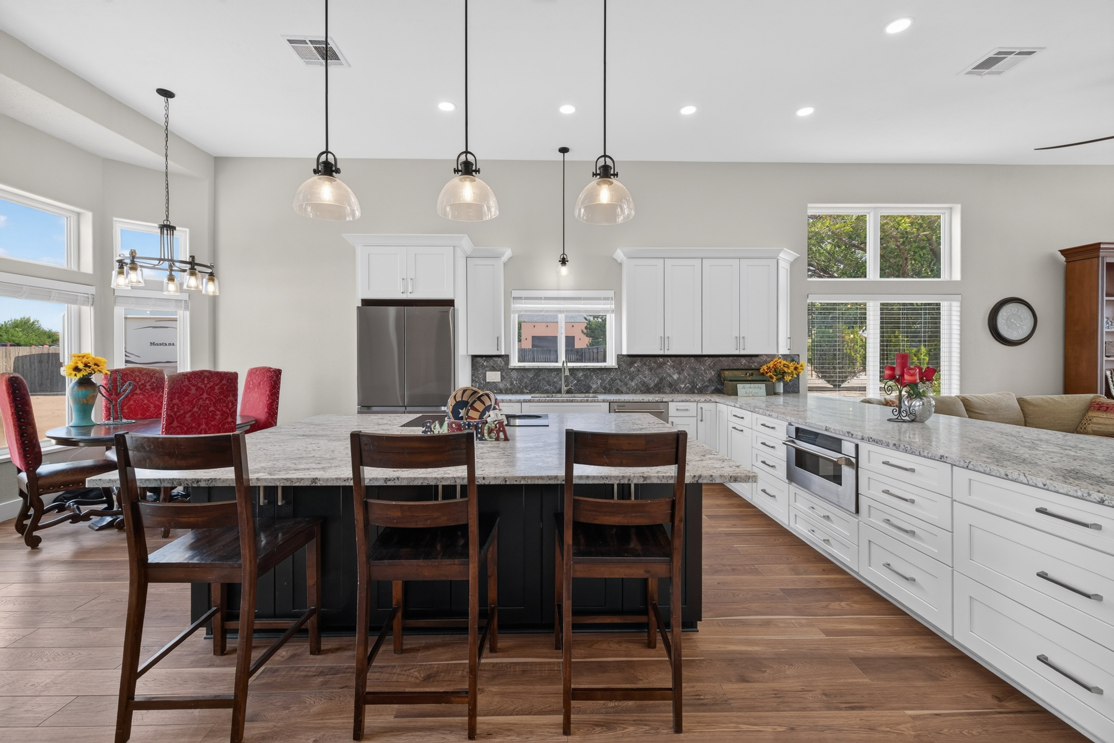 Spacious kitchen featuring an extended island with stone countertops, white cabinetry with dark hardware, stainless steel appliances, wood-finish flooring, and pendant lighting