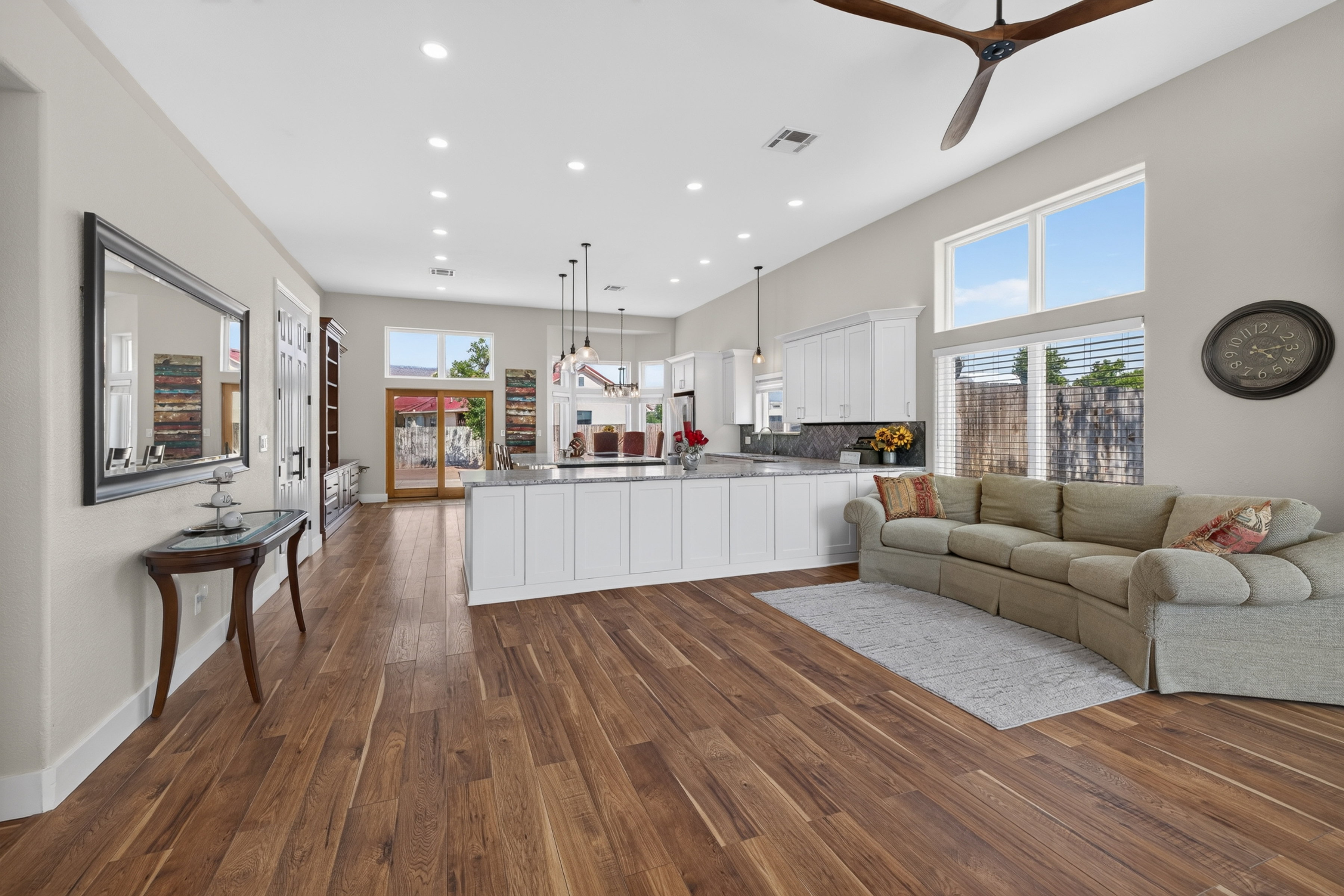 Spacious open-concept interior featuring wood-finish flooring throughout, a large kitchen island with a stone countertop, white shaker-style cabinetry, and high ceilings with recessed lighting