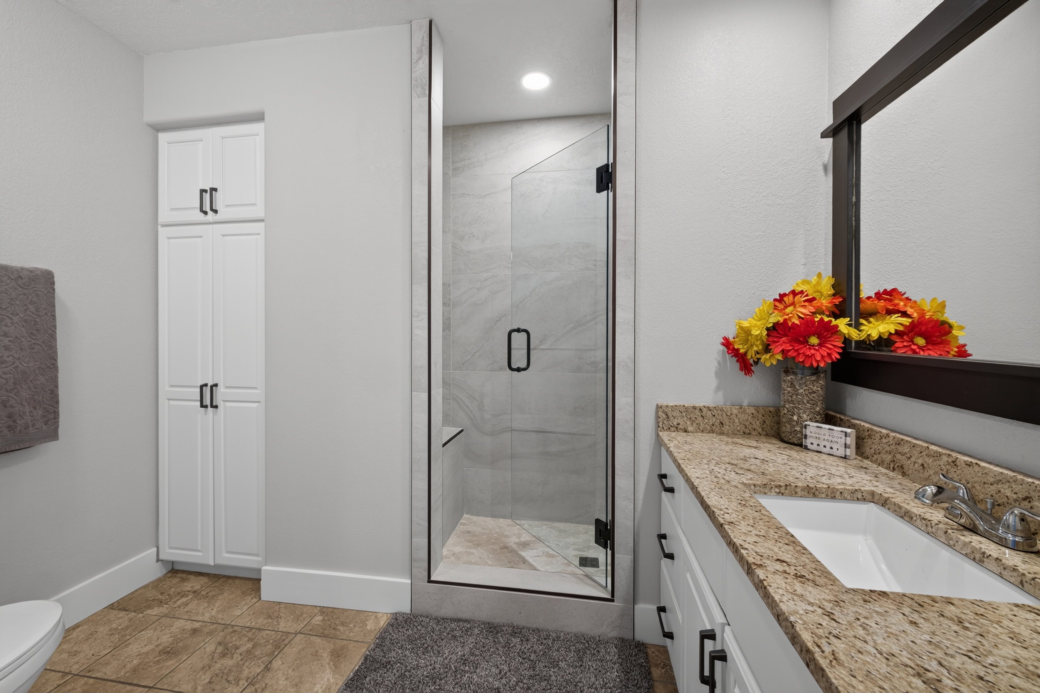 Bathroom featuring a glass-enclosed shower with tile surround, a single vanity with stone countertop, white cabinetry with dark hardware, and tile flooring