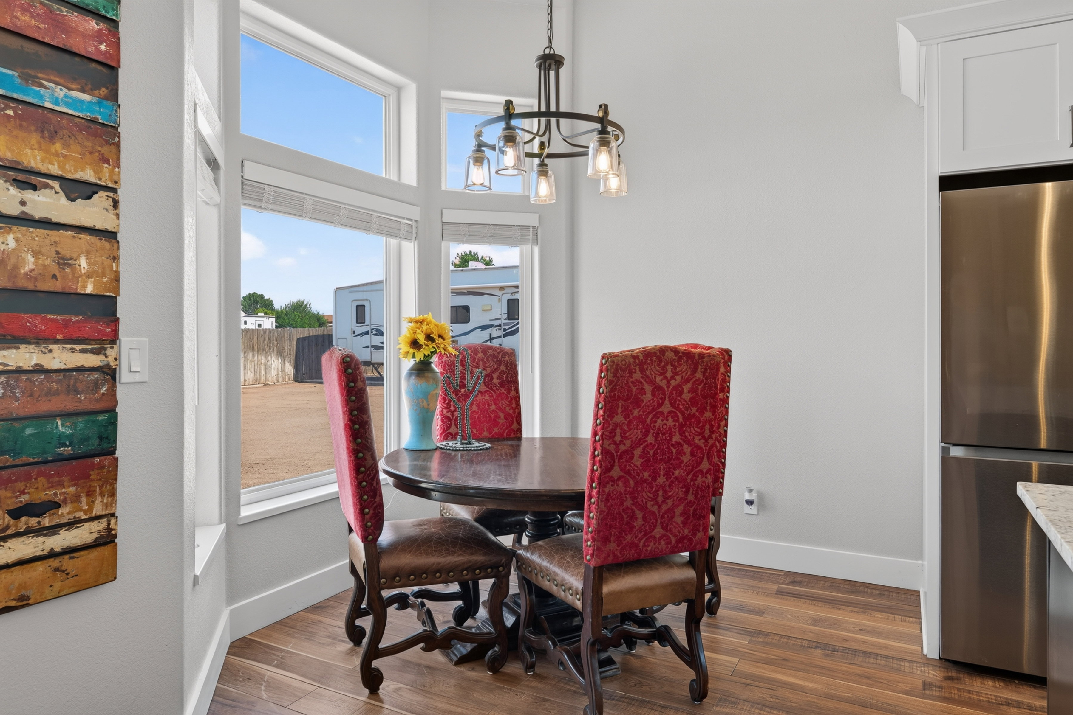 Dining nook featuring a bay window, wood-finish flooring, a built-in stainless steel refrigerator, and an overhead chandelier with clear glass shades