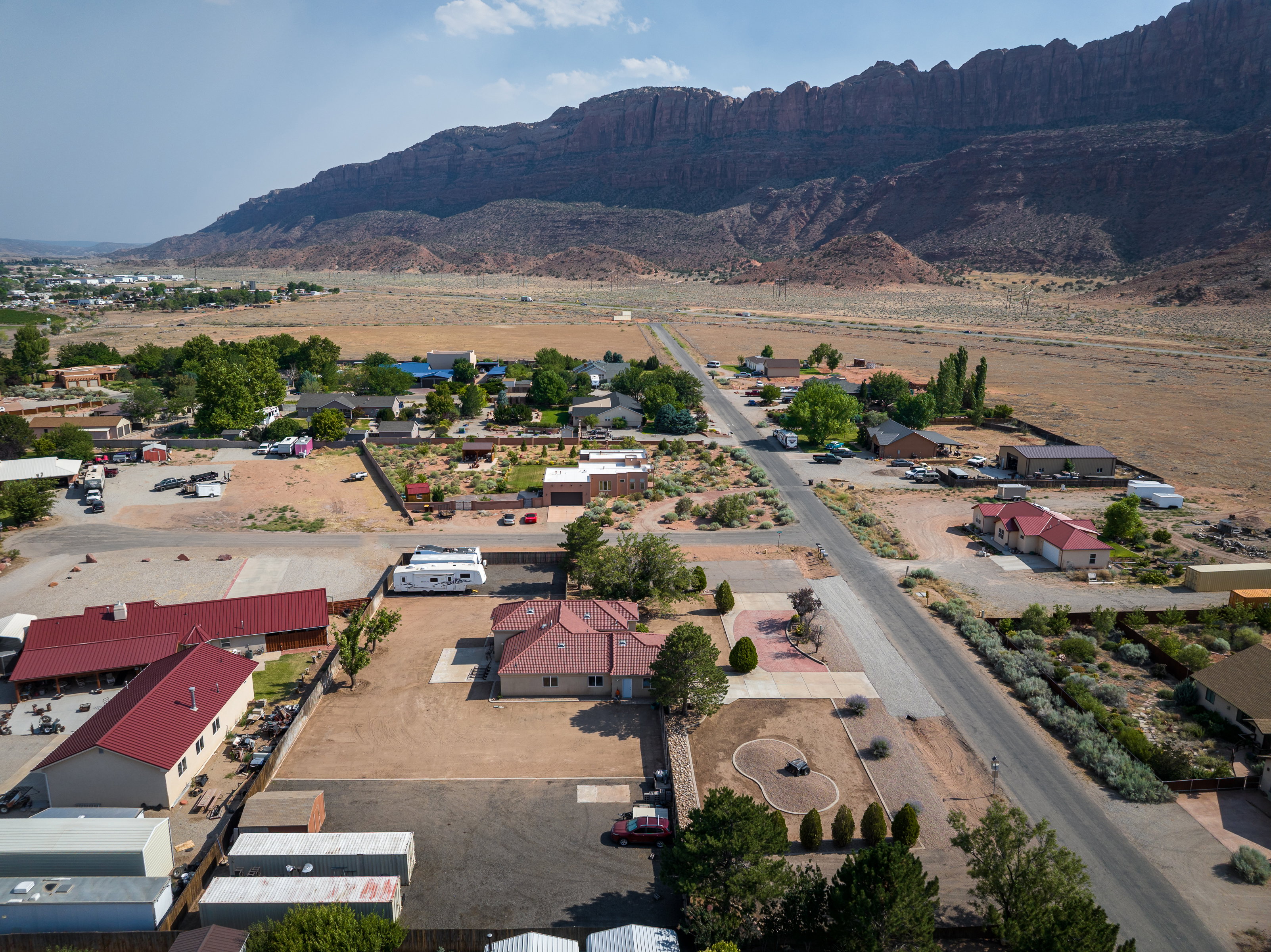 Aerial perspective showcasing multiple properties, with a prominent red-roofed residence featuring an expansive paved driveway